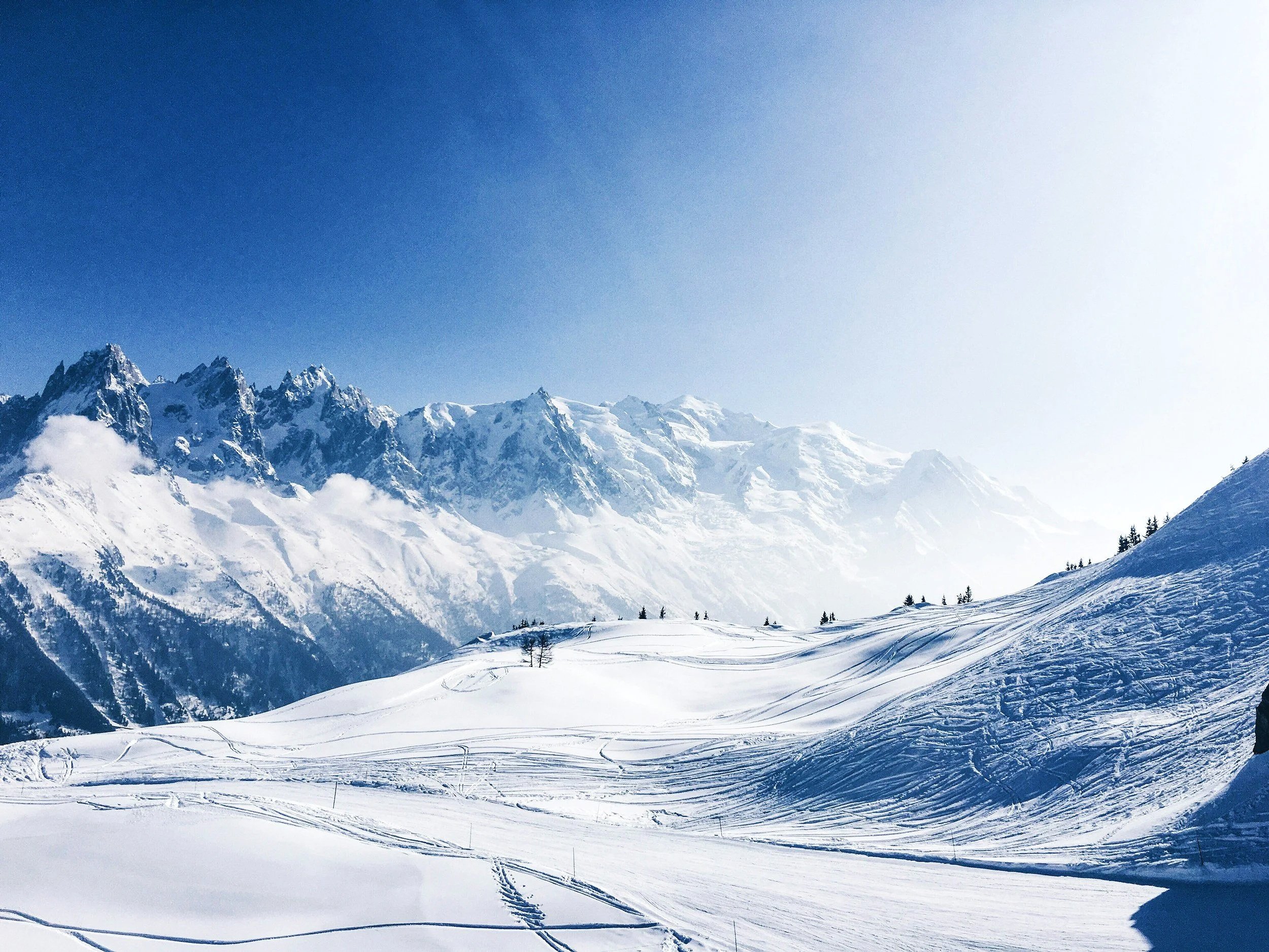 Snow-covered mountain range under a clear blue sky with ski tracks on the slopes.