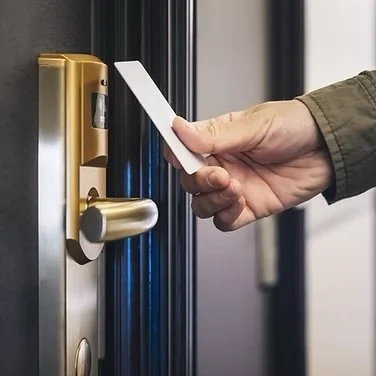 Person inserting a key card into a gold digital door lock on a black door.
