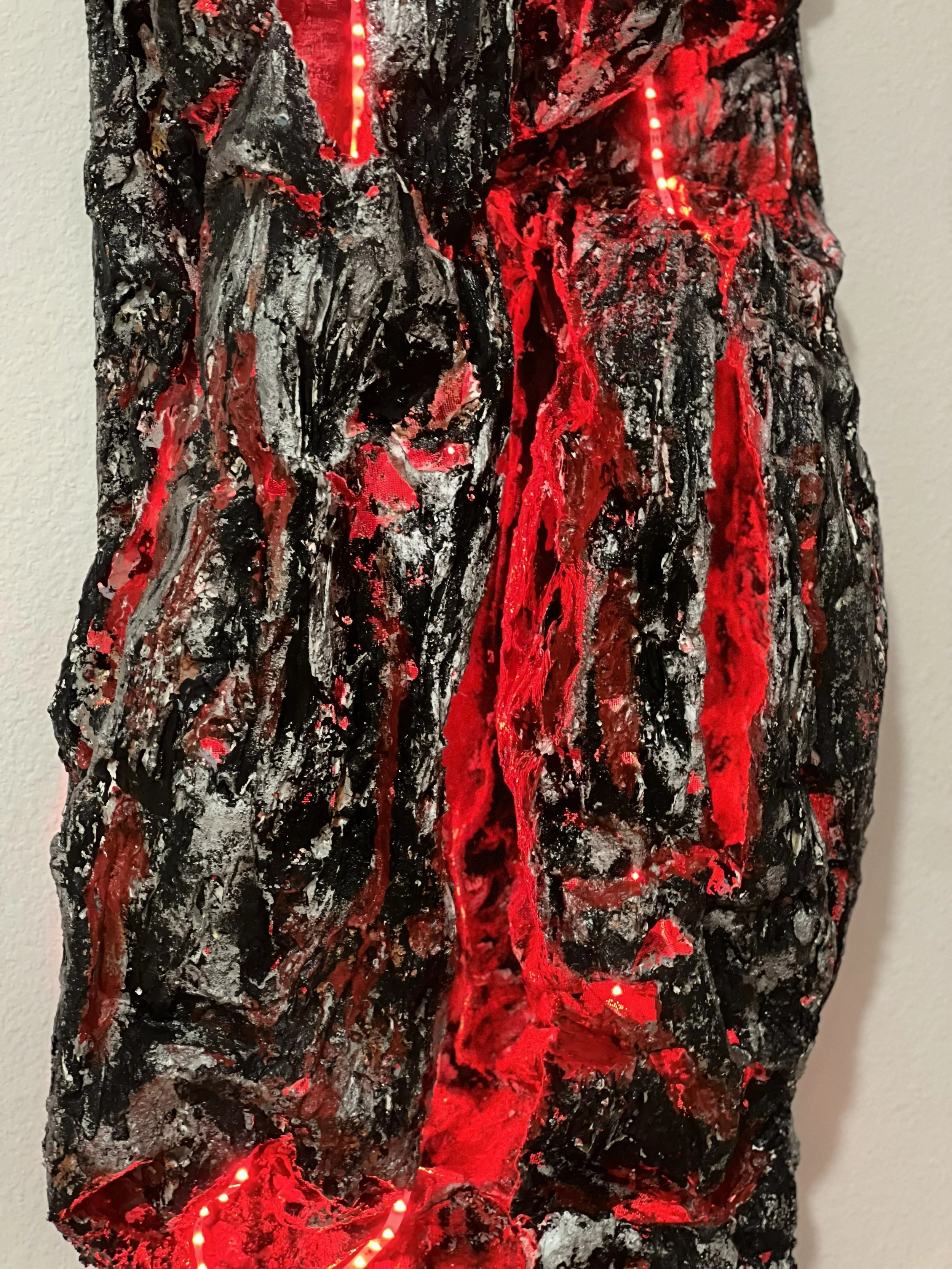 Close-up of a textured, black and red sculpture or artwork with a rough surface, illuminated with small red LED lights woven into the piece.