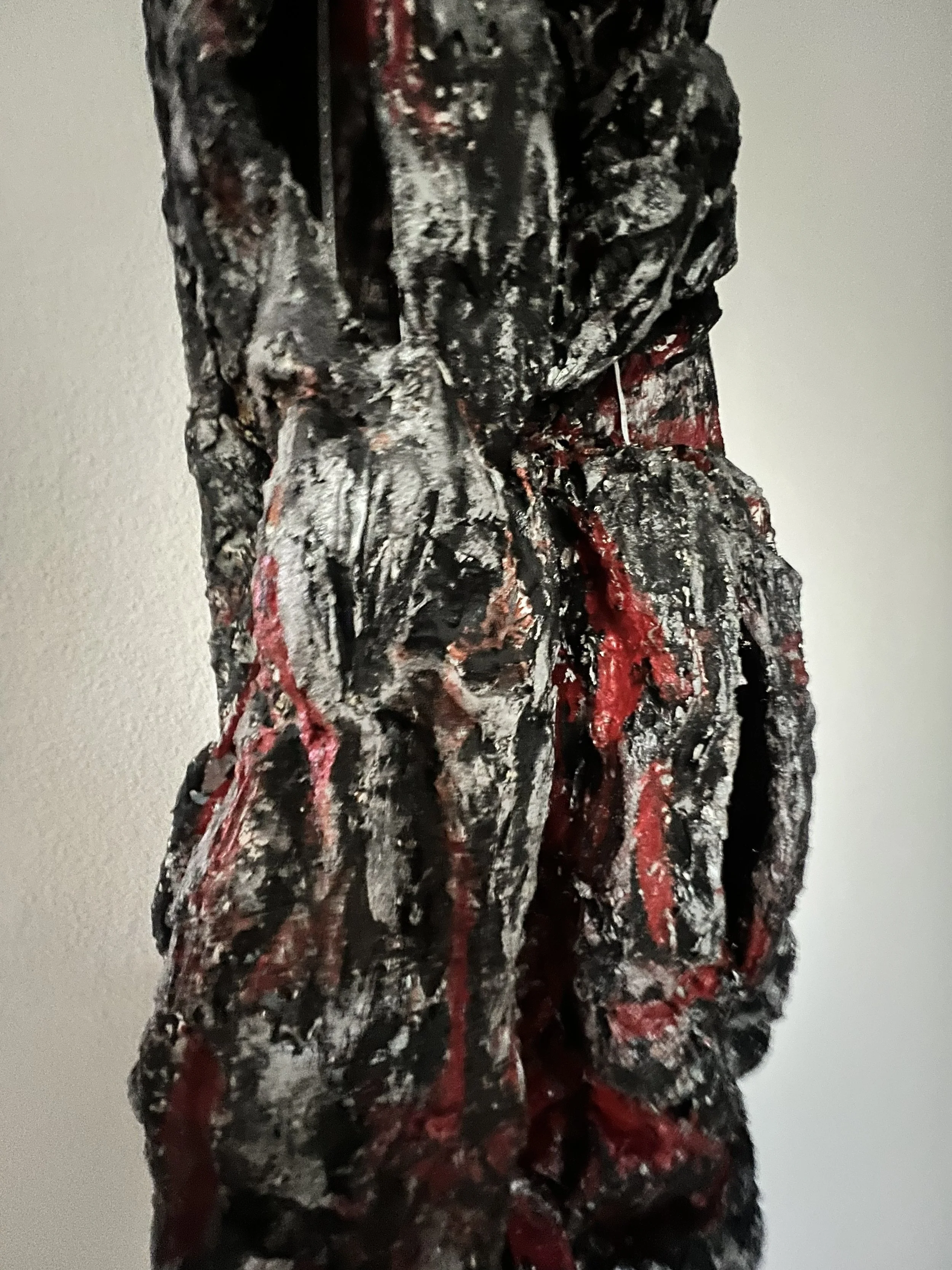Close-up of an abstract painting with black, red, white, and gray textured paint on a vertical surface.