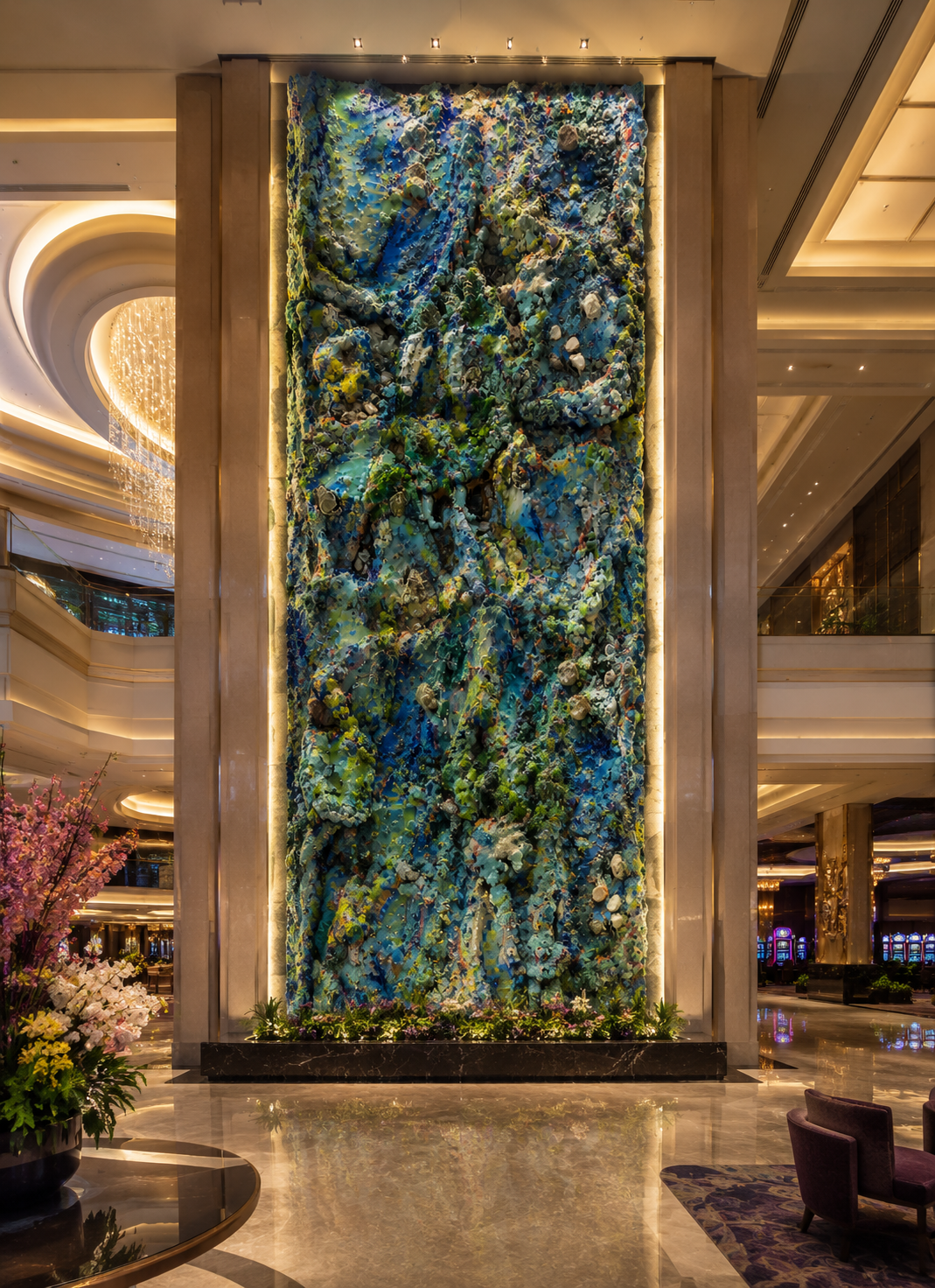 A tall, colorful abstract art installation made of textured materials displayed on a wall in a luxurious hotel lobby