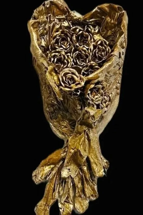 A bouquet made of gold-colored metallic roses wrapped in gold foil against a black background.