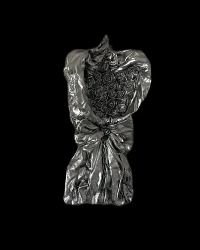 A bouquet of roses wrapped in metallic silver paper, against a black background.