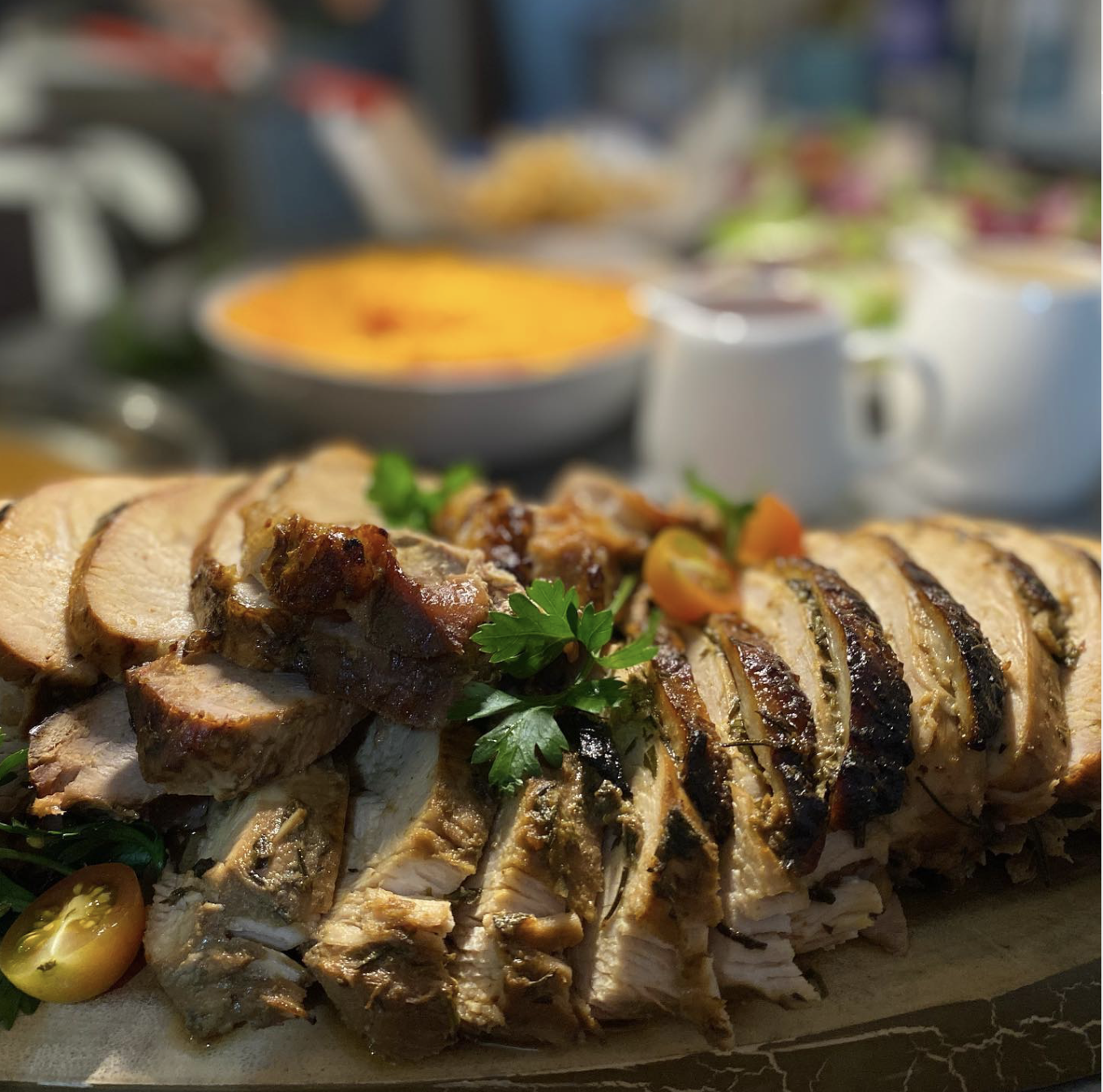 Pavo y cerdo rostizado en rebanadas con verduras y perejil, fondo con platos y tazas