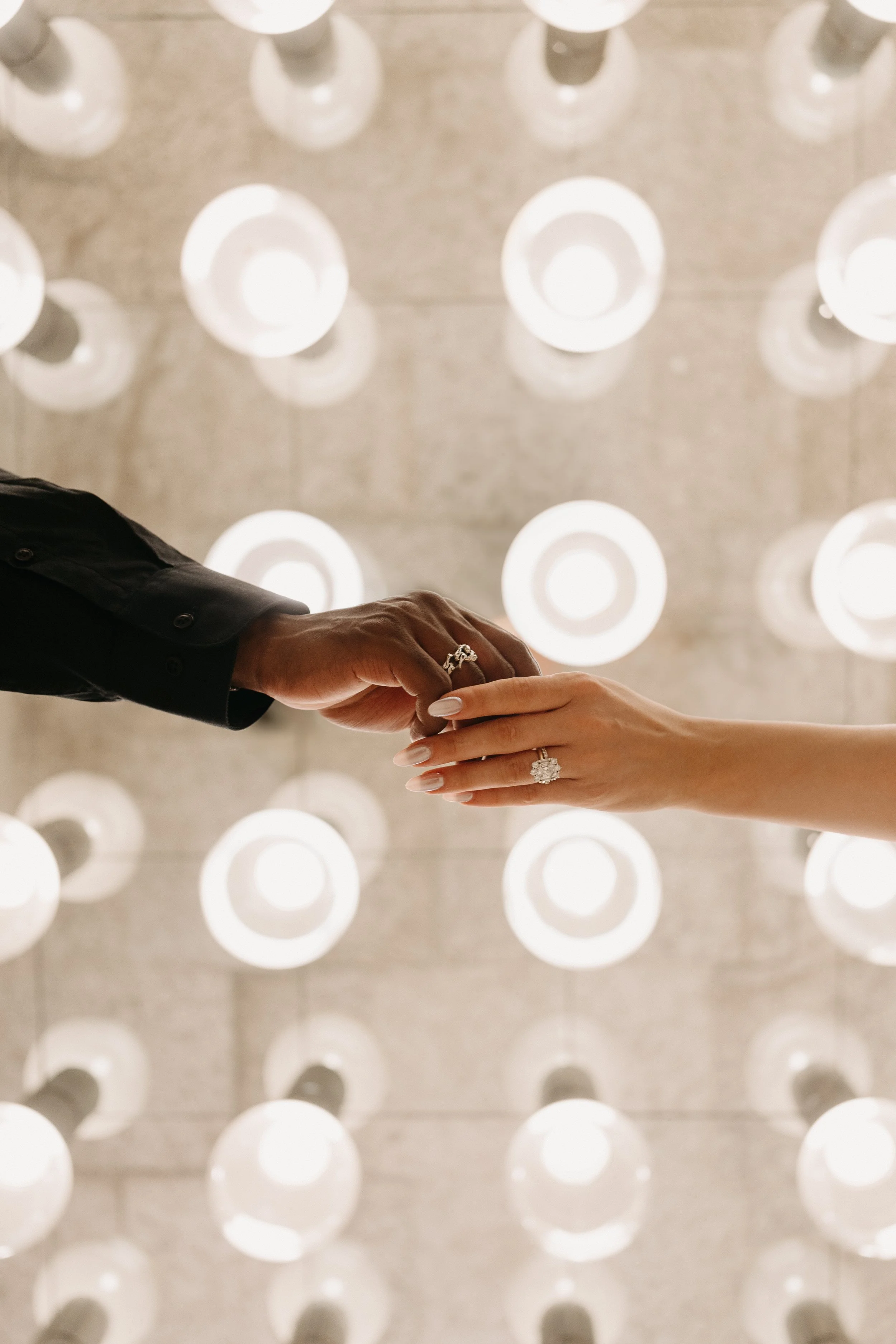 A Bride and Groom hold hands below vintage lights at Winnipeg Art Gallery