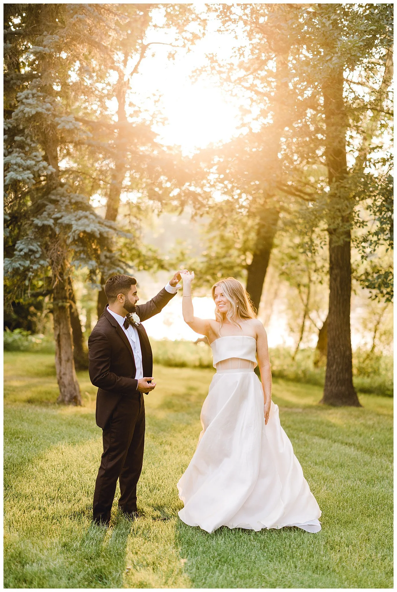 Groom spins bride candidly as they dance at sunset.