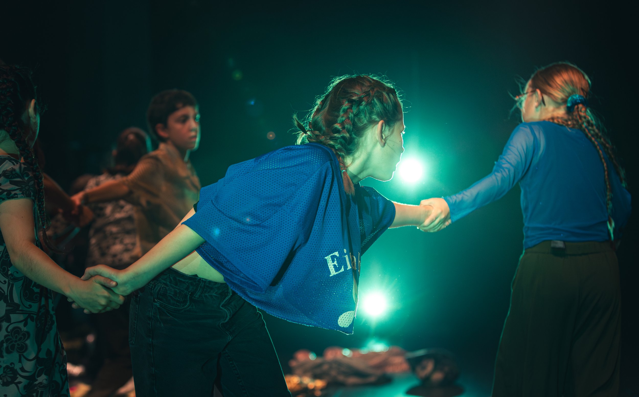 Des enfants, dont deux filles en chemises bleues, se tiennent par la main, se tenant la main lors d'une scène dramatique sous un éclairage vert. L'un des enfants s'incline pour serrer la main d'une autre fille.