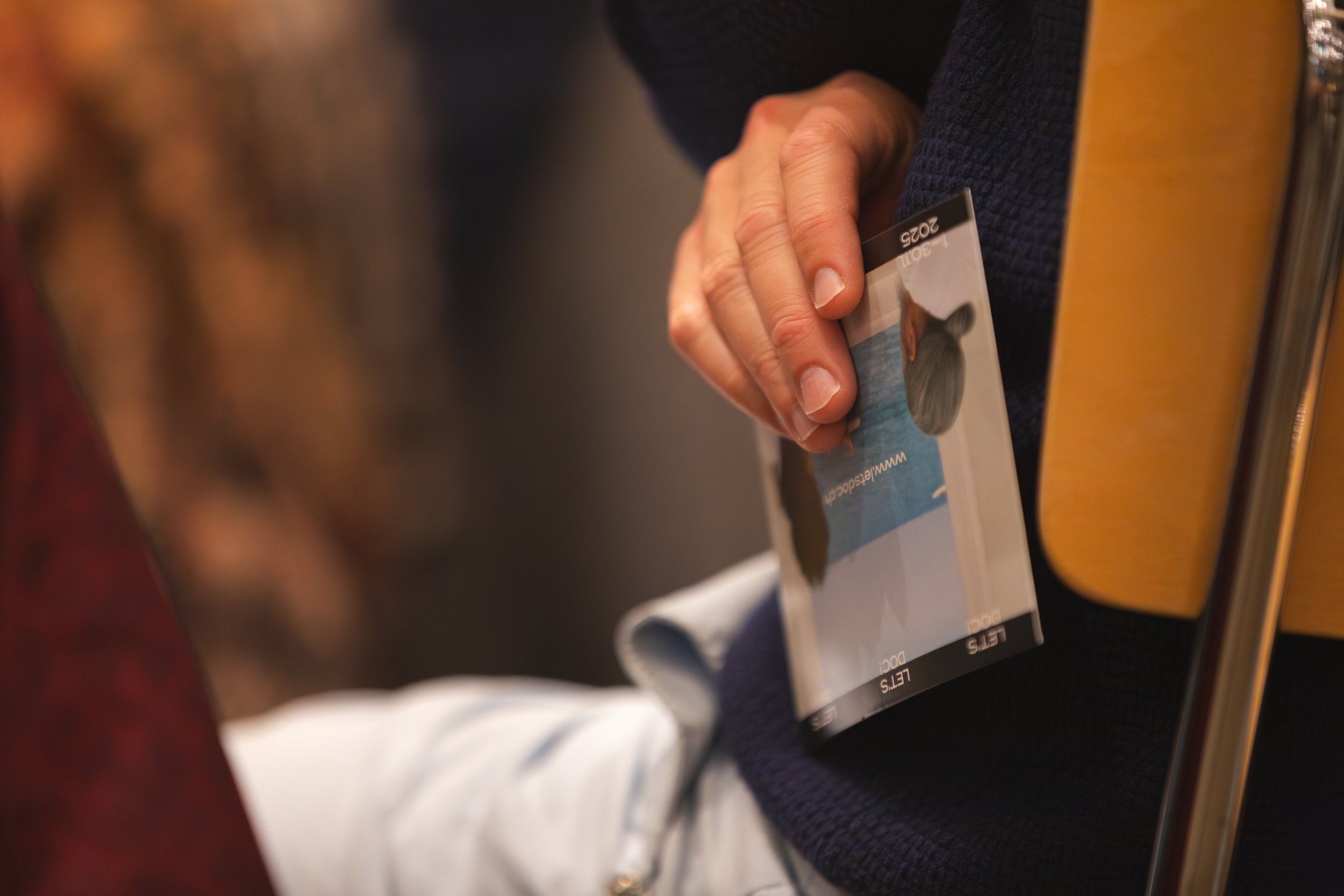 Une main tenant une carte de transport ou de train dans une rame de métro ou de train, avec un siège jaune visible à côté.
