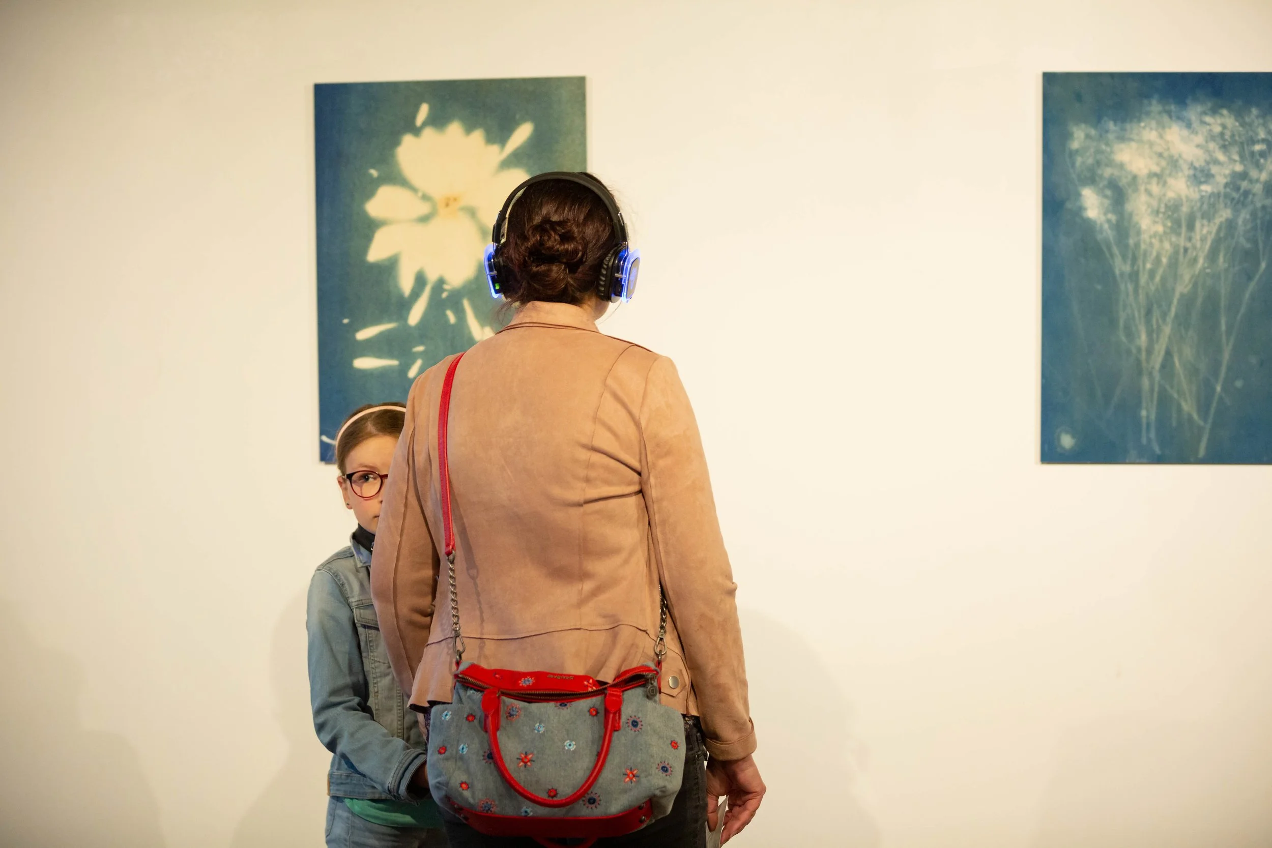 Une femme portant un casque d'écoute regarde deux tableaux dans une galerie d'art, une fillette la regarde.