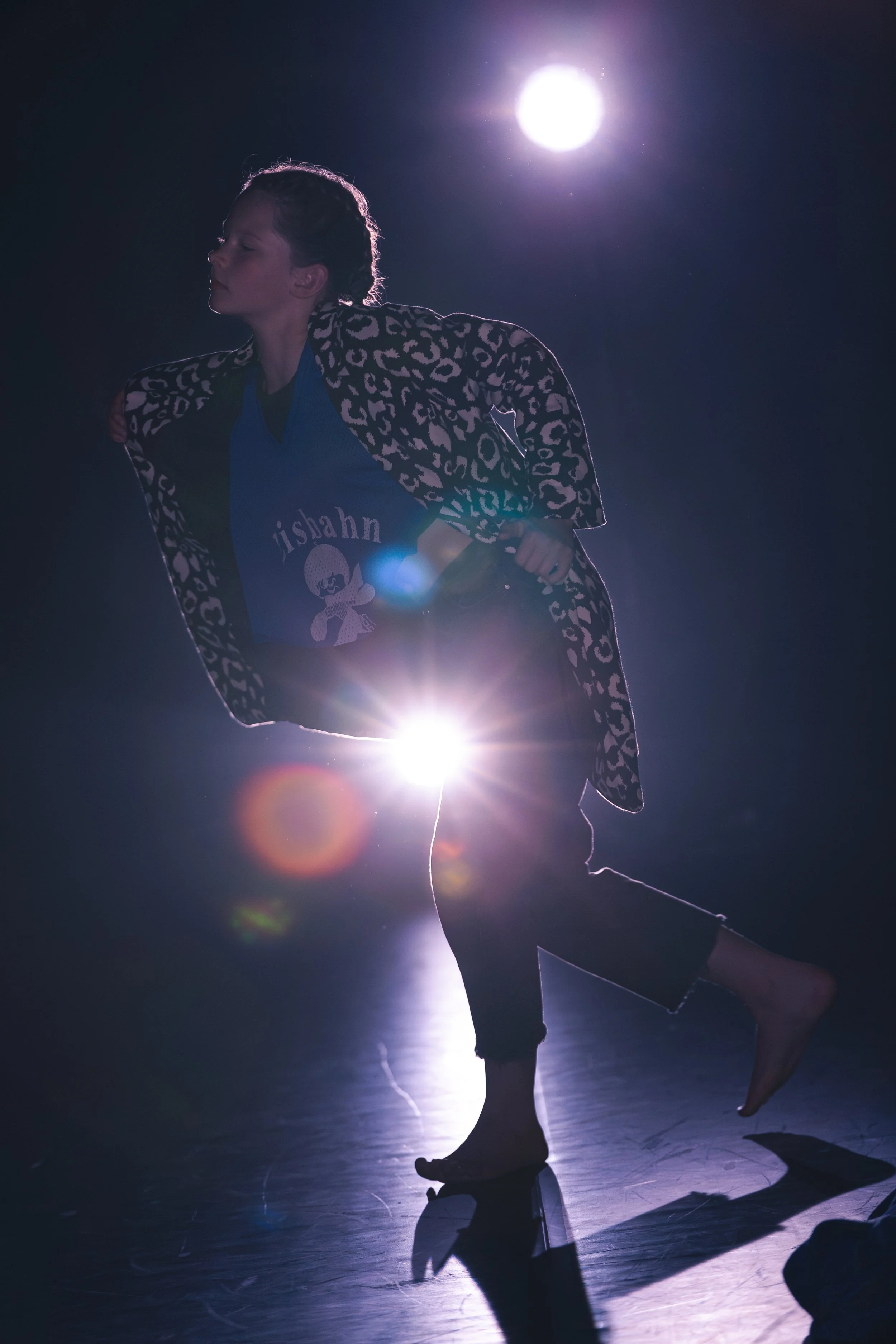 Une personne danse dans un studio avec un éclairage intense derrière elle, créant des silhouettes et un effet de contre-jour.