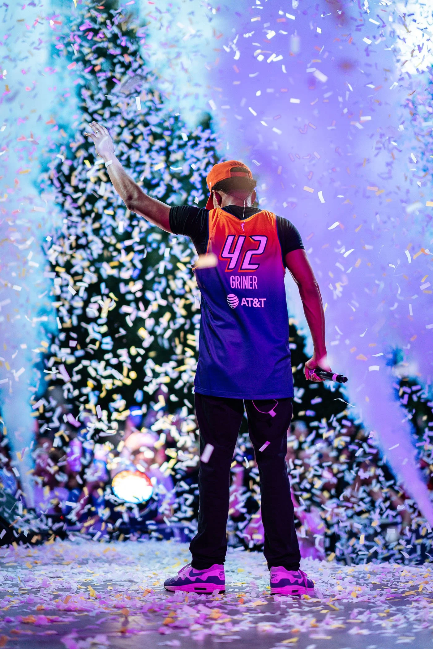 Chance The Rapper standing on stage with confetti falling arounds, wearing a sports jersey with the number 42, holding a microphone, at a celebration or event.