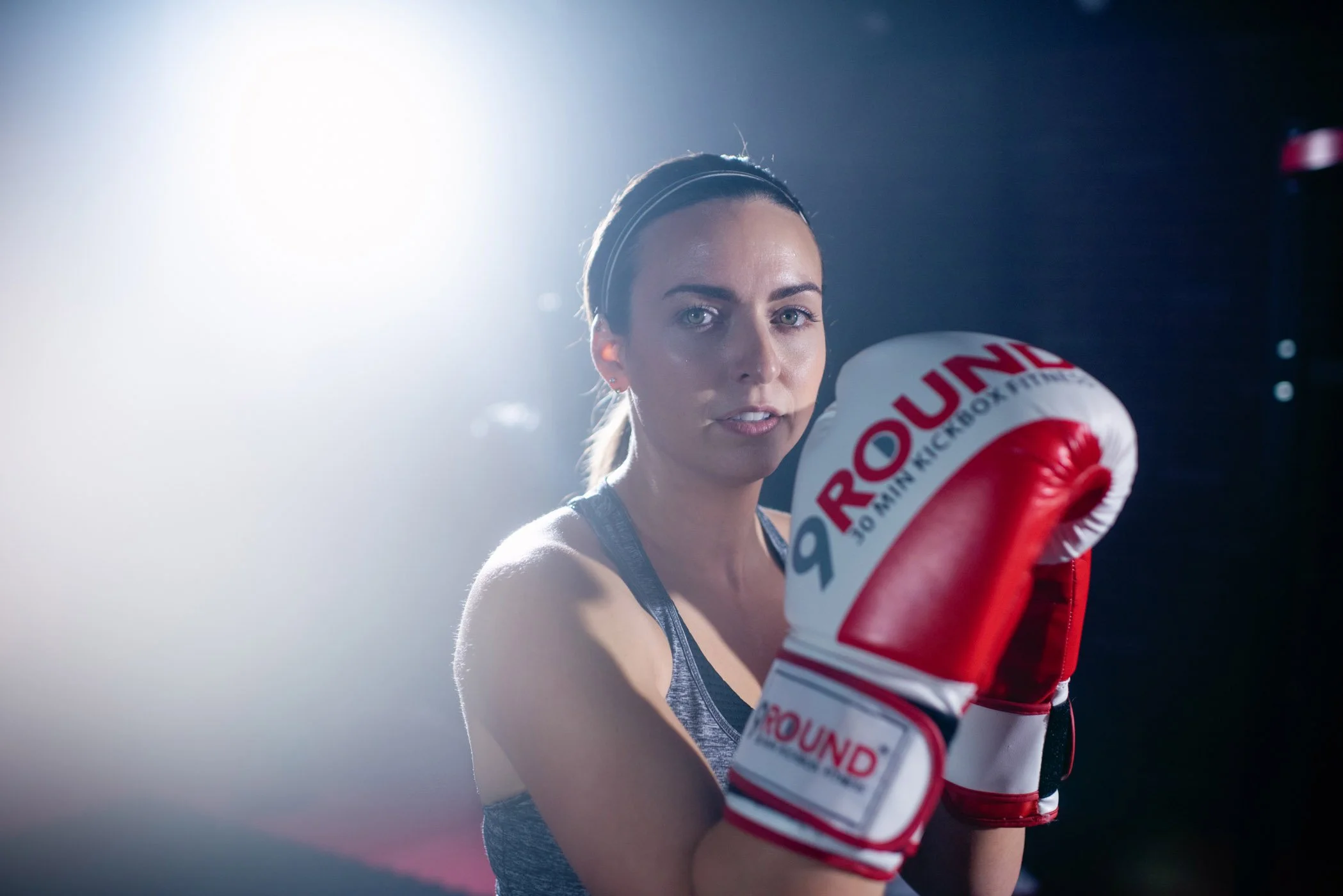 A campaign for 9Round featuring a female athlete in athletic clothing wearing boxing gloves in a gym