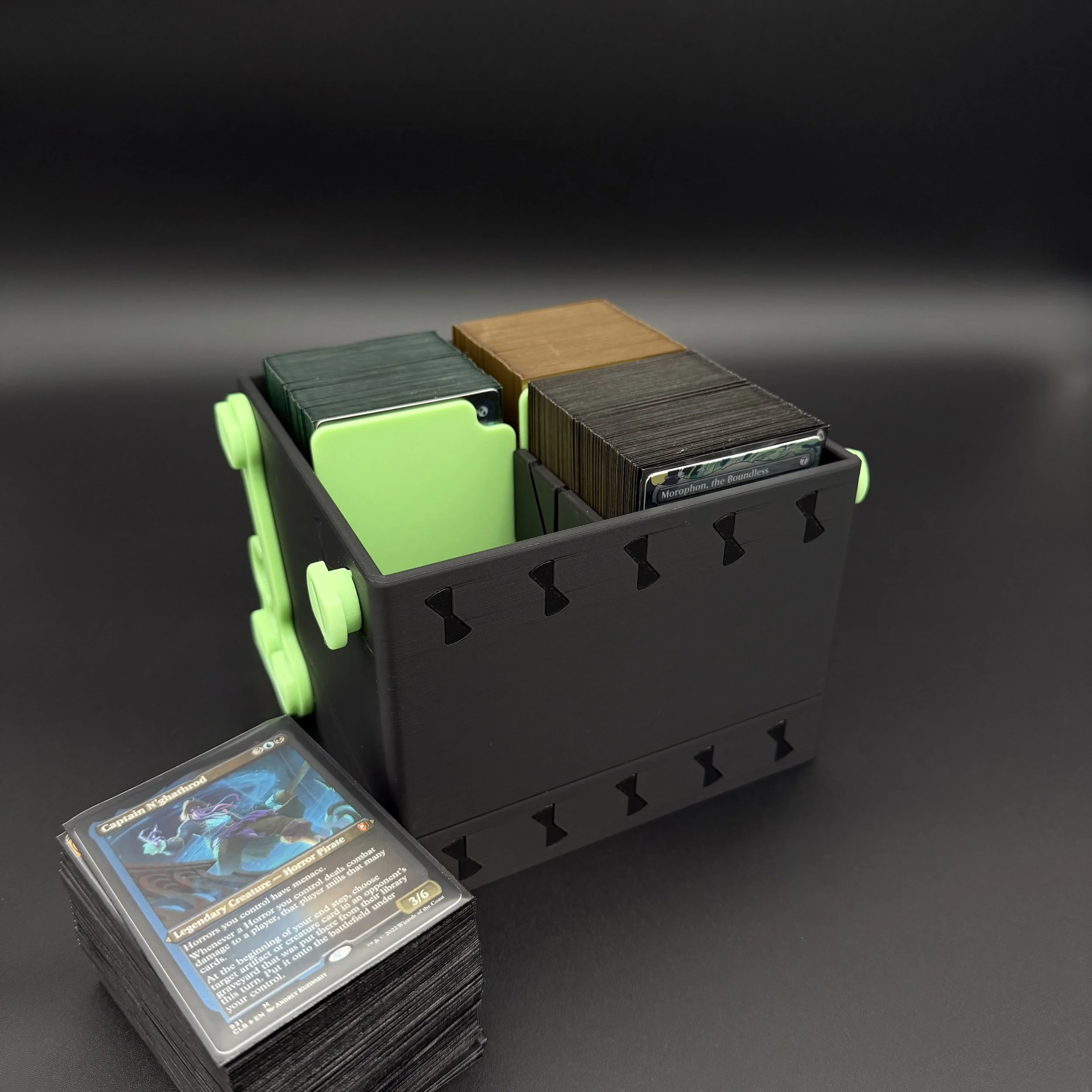 A black and glow in the dark green deckbox shown with its lid stored underneath it.
