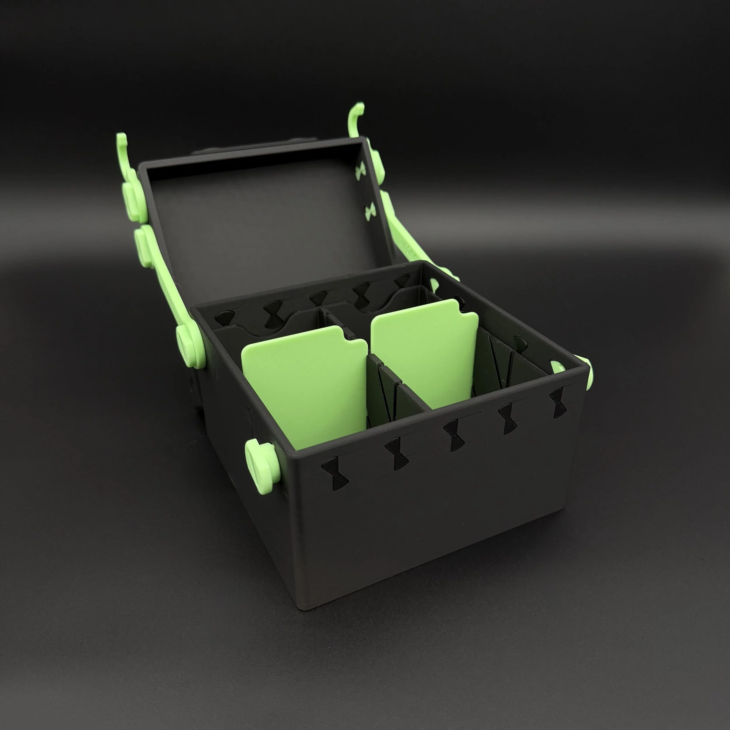 A black and glow in the dark green deckbox shown with its lid open, displaying its black and green internal dividers.