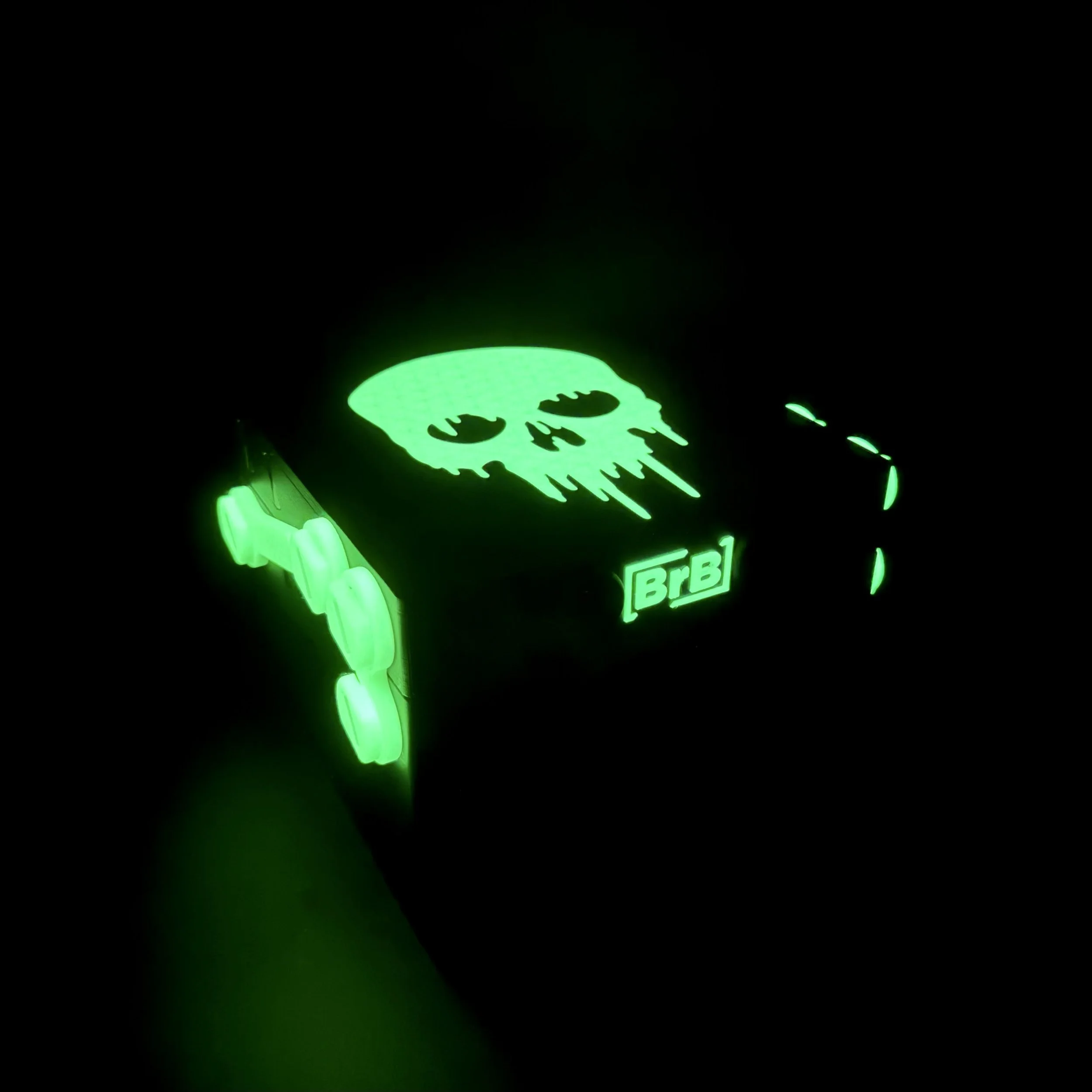 A black deckbox with a glow in the dark skull on the lid, shown with the lights off and glowing.