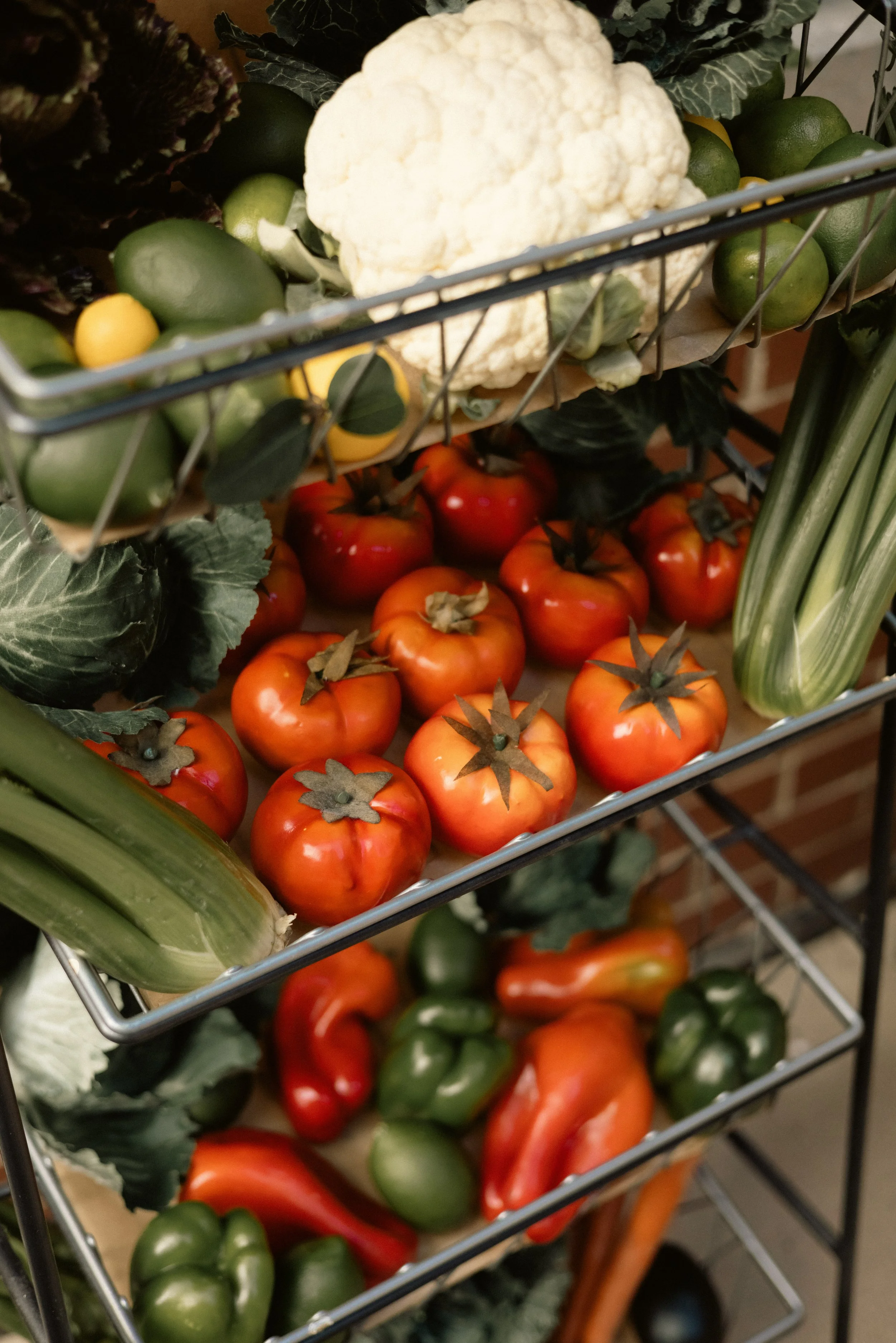 Basket containing cauliflower, yellow cherry tomatoes, green avocados, red bell peppers, and other vegetables.