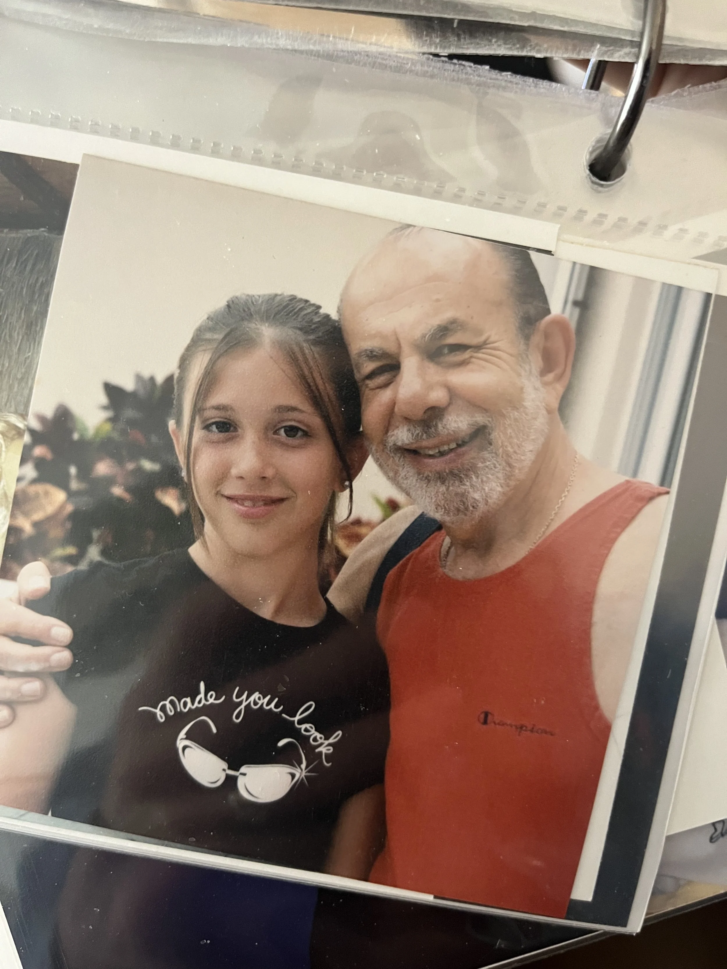 A young woman and an older man are close together, smiling for a selfie. The woman has brown hair, and the man has a beard and is wearing a red sleeveless shirt. The woman is holding a phone to take the picture, and they are indoors with blurred background. The text on the photo reads "made you look" and has an image of pair of glasses.