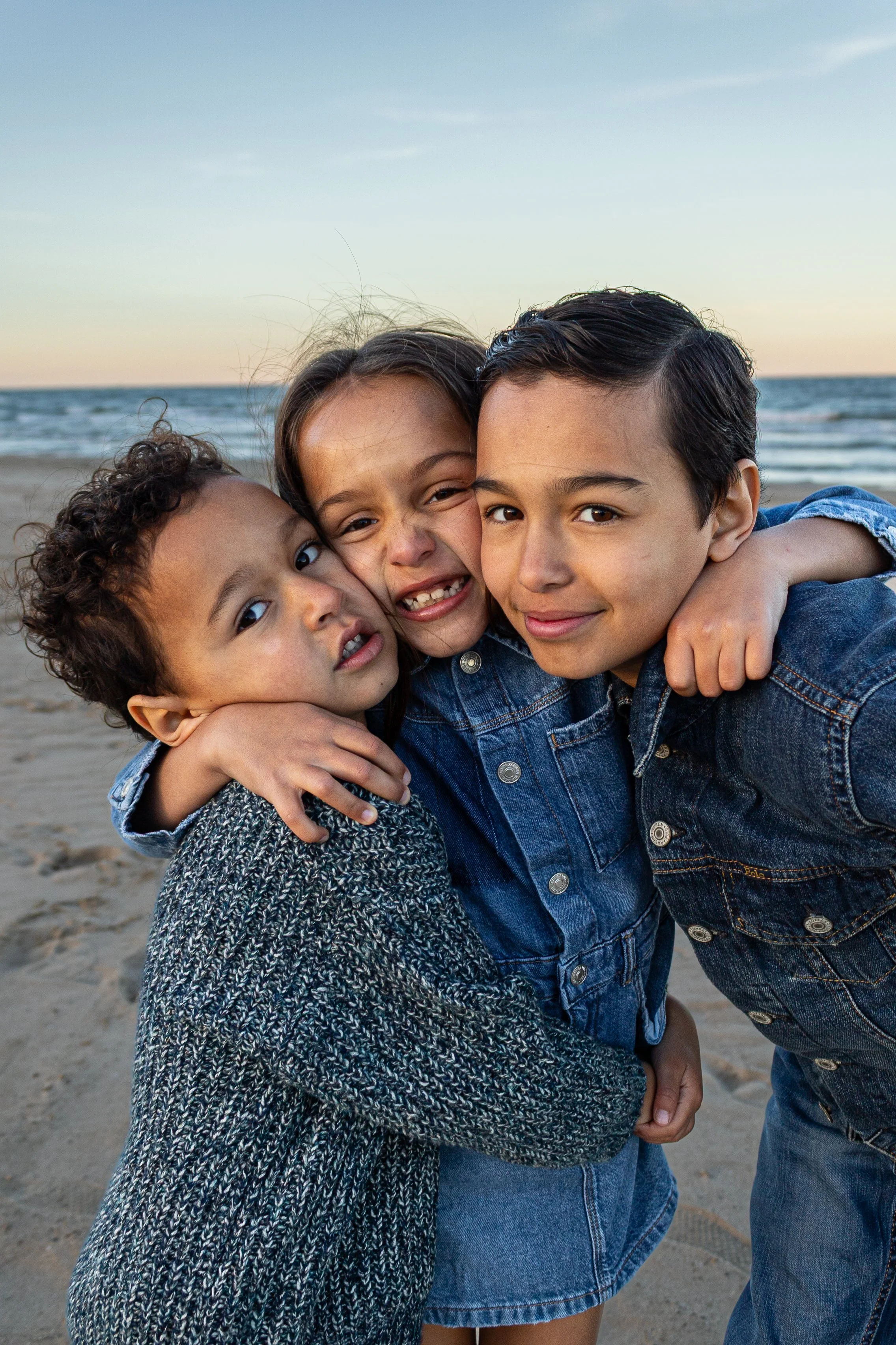 Three children hugging each other on the beach during sunset.
