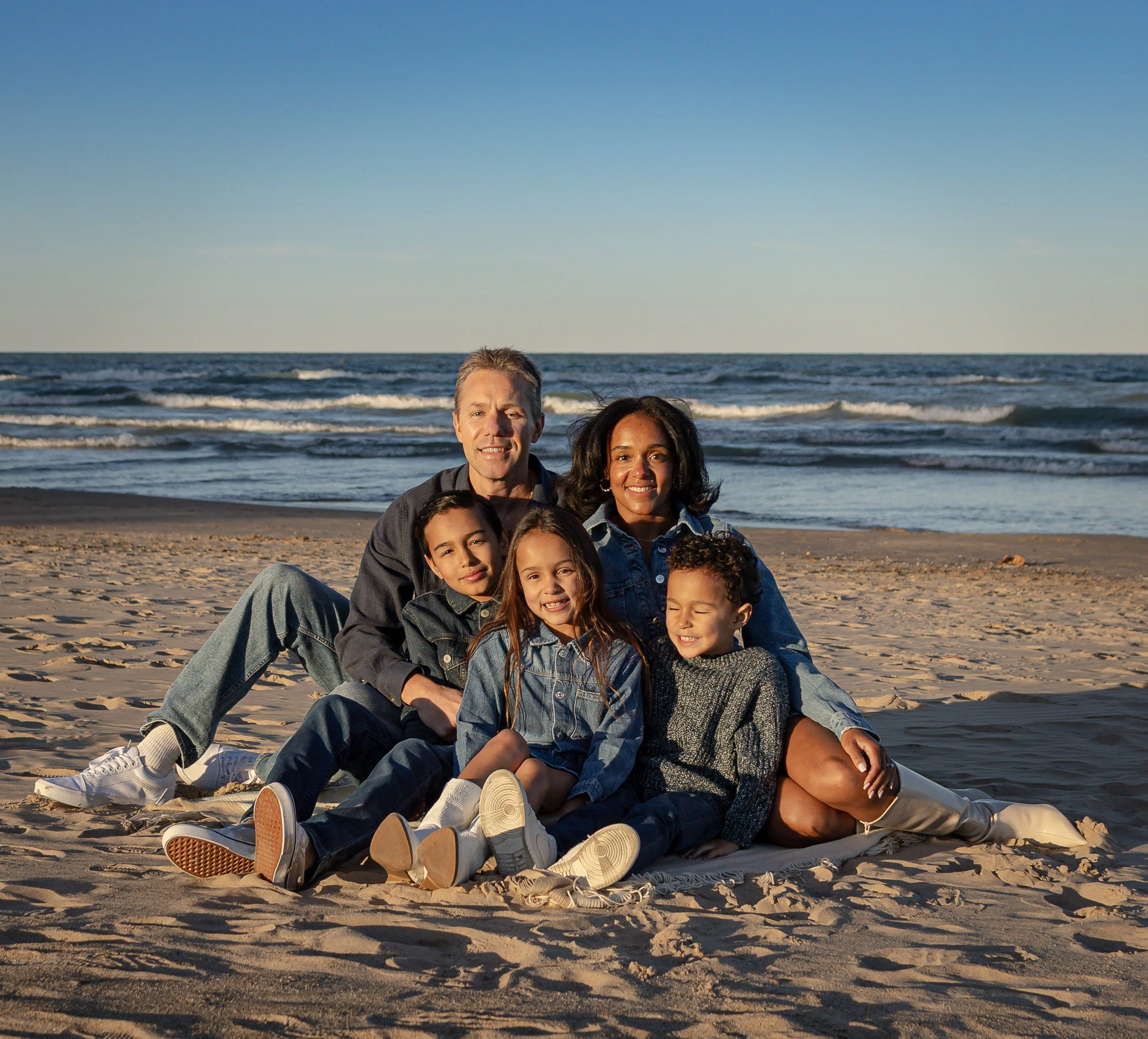 Group of six people sitting on the beach with ocean waves in the background during sunset or late afternoon.