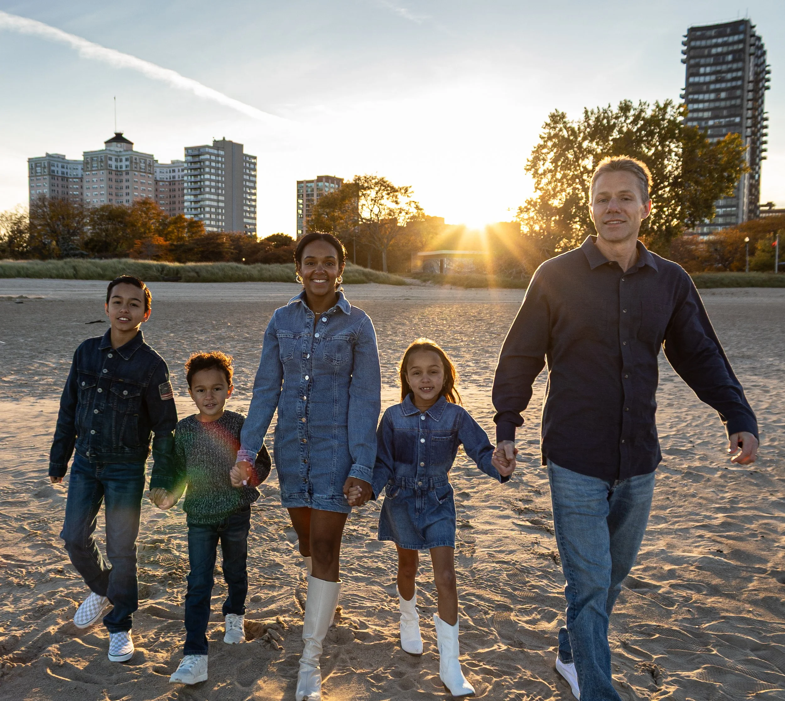 Family of six walking on the beach during sunset, with city buildings in the background.
