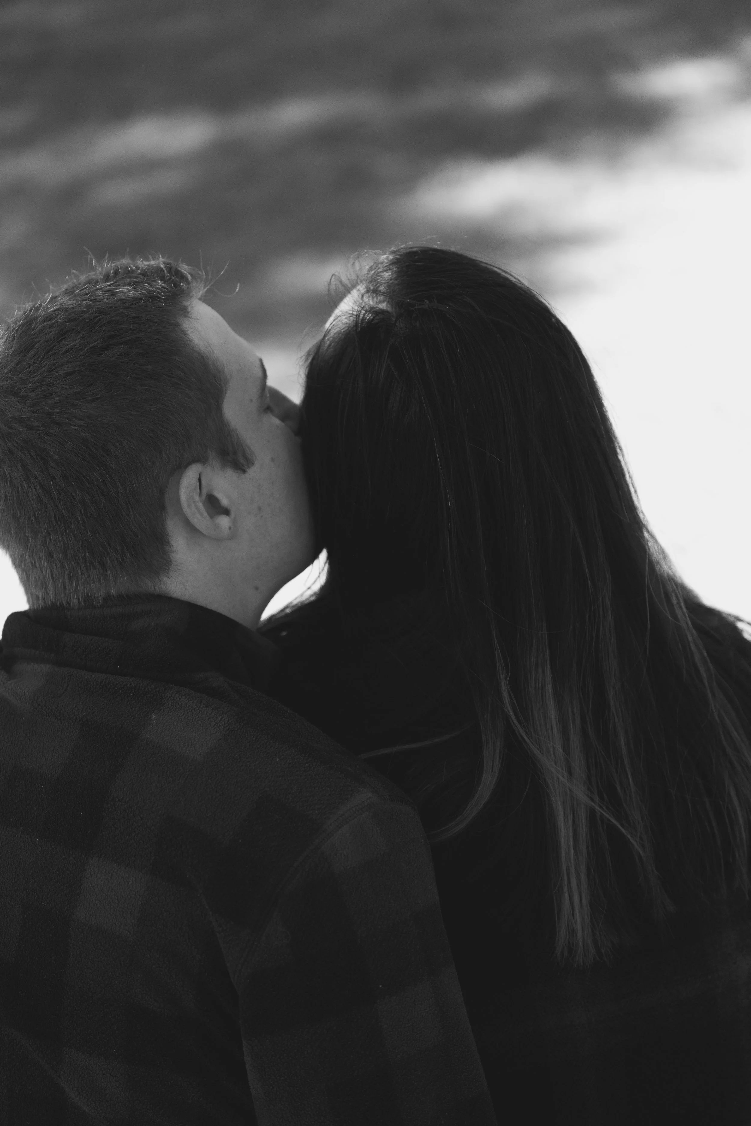 A black and white close-up photo of a couple kissing, with the man's face in profile and the woman's head turned towards him, guitar in the background.