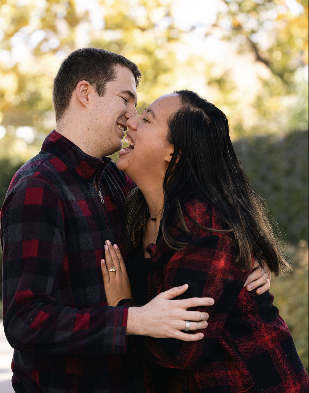 A happy couple embracing and laughing outdoors in a park with autumn trees in the background.
