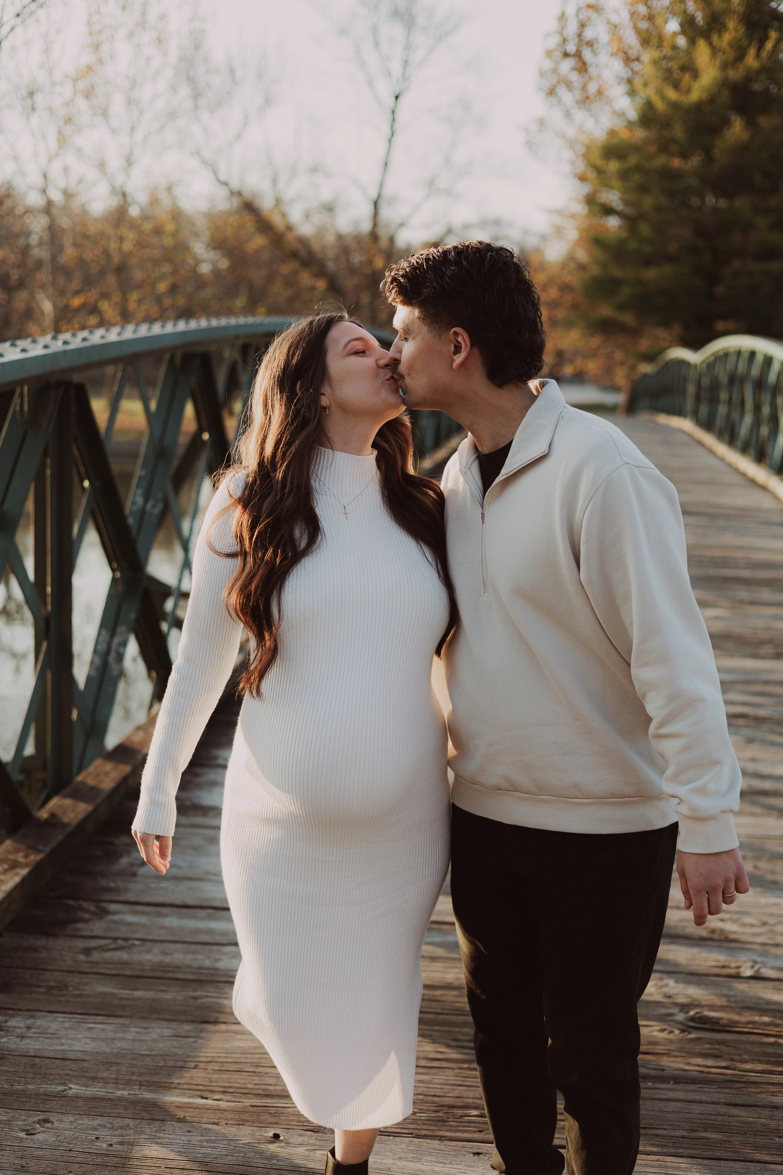 A couple sharing a kiss on a wooden bridge during autumn with trees in the background.