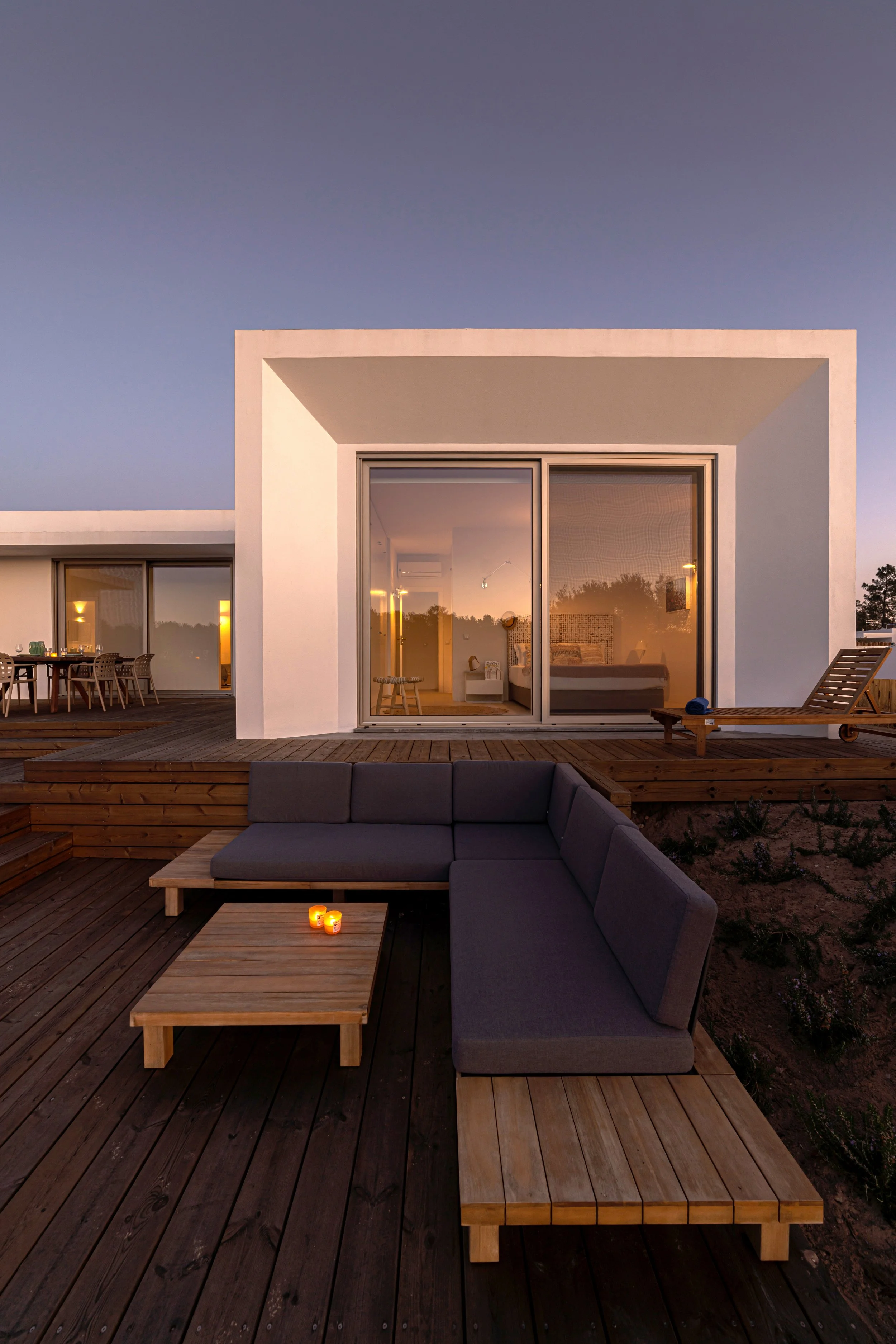 Modern house with large glass sliding door, rooftop deck with outdoor seating, candles, and a panoramic view at dusk.