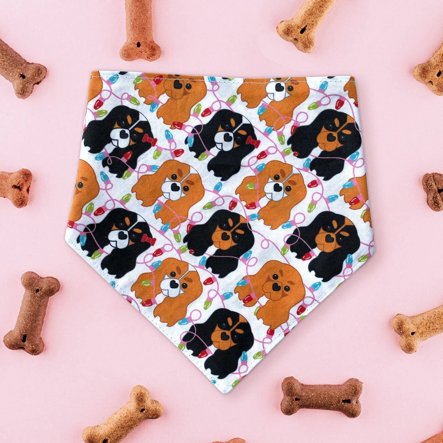Bandana featuring a pattern of Cavalier King Charles Spaniels and Christmas bulbs on a pink background surrounded by dog bones