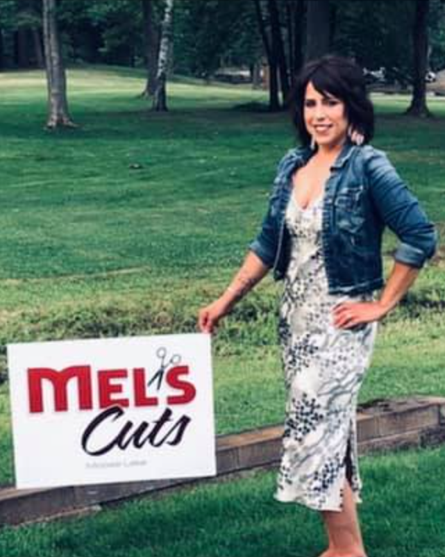 Melissa Anderson holding a Mel's Cuts sign.