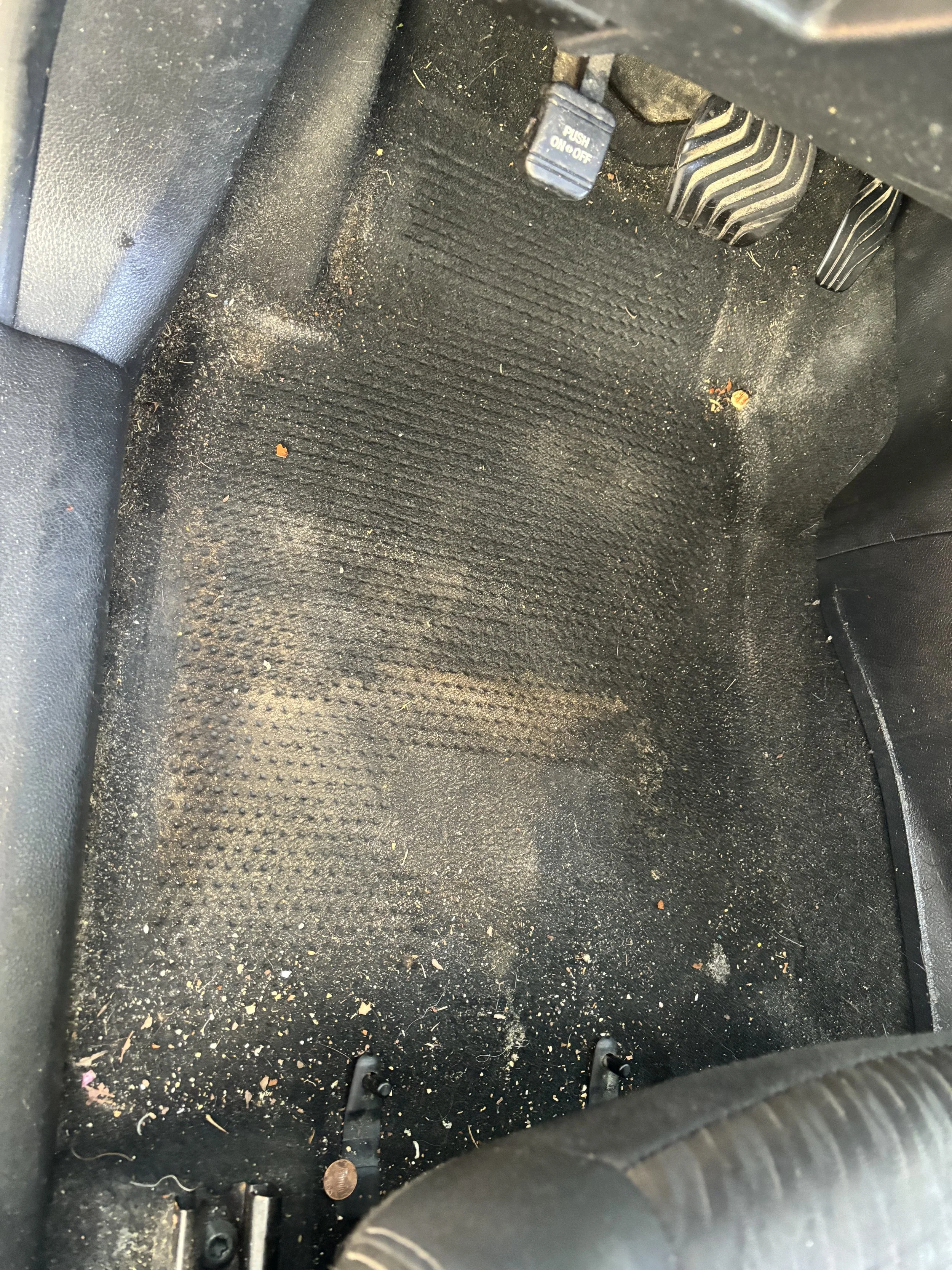 Dirty car floor interior with heavy debris and buildup before auto detailing service in DeLand FL.