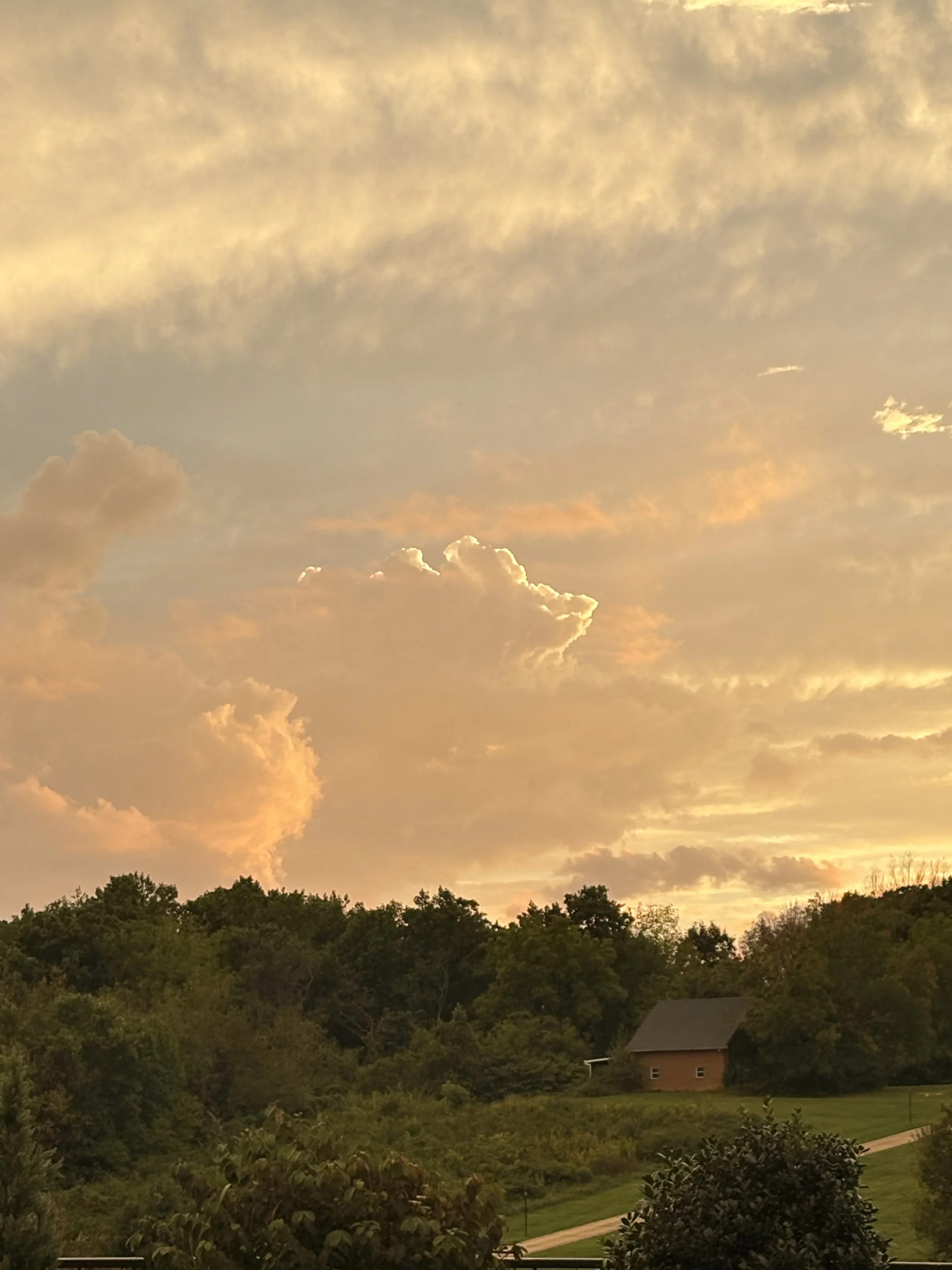 A sunset sky with orange and yellow clouds over a green landscape with trees and a small brick house.