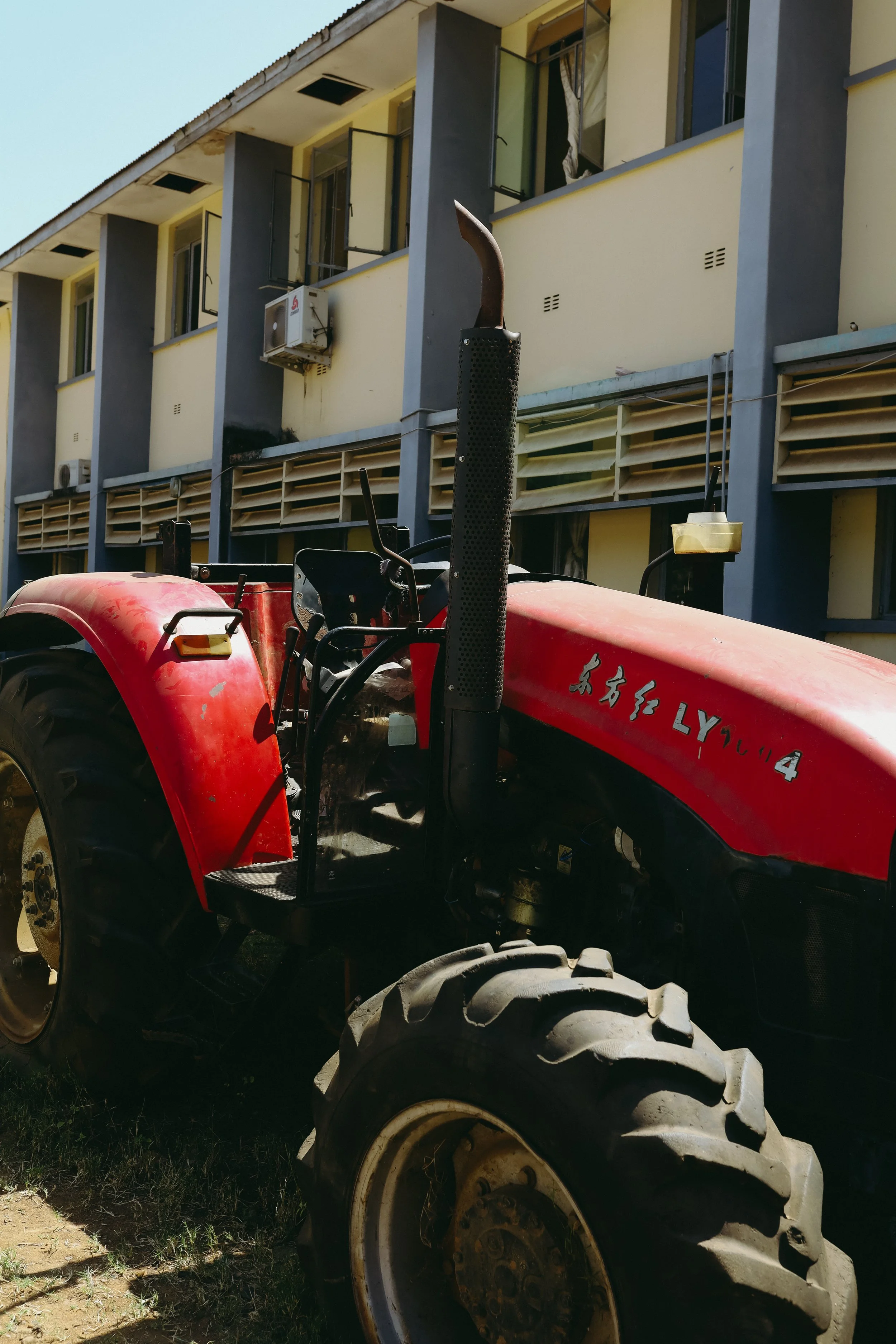 Close-up of a red tractor with Chinese characters and the number 'LY04' on its side, parked outdoors with a multi-story apartment building in the background.