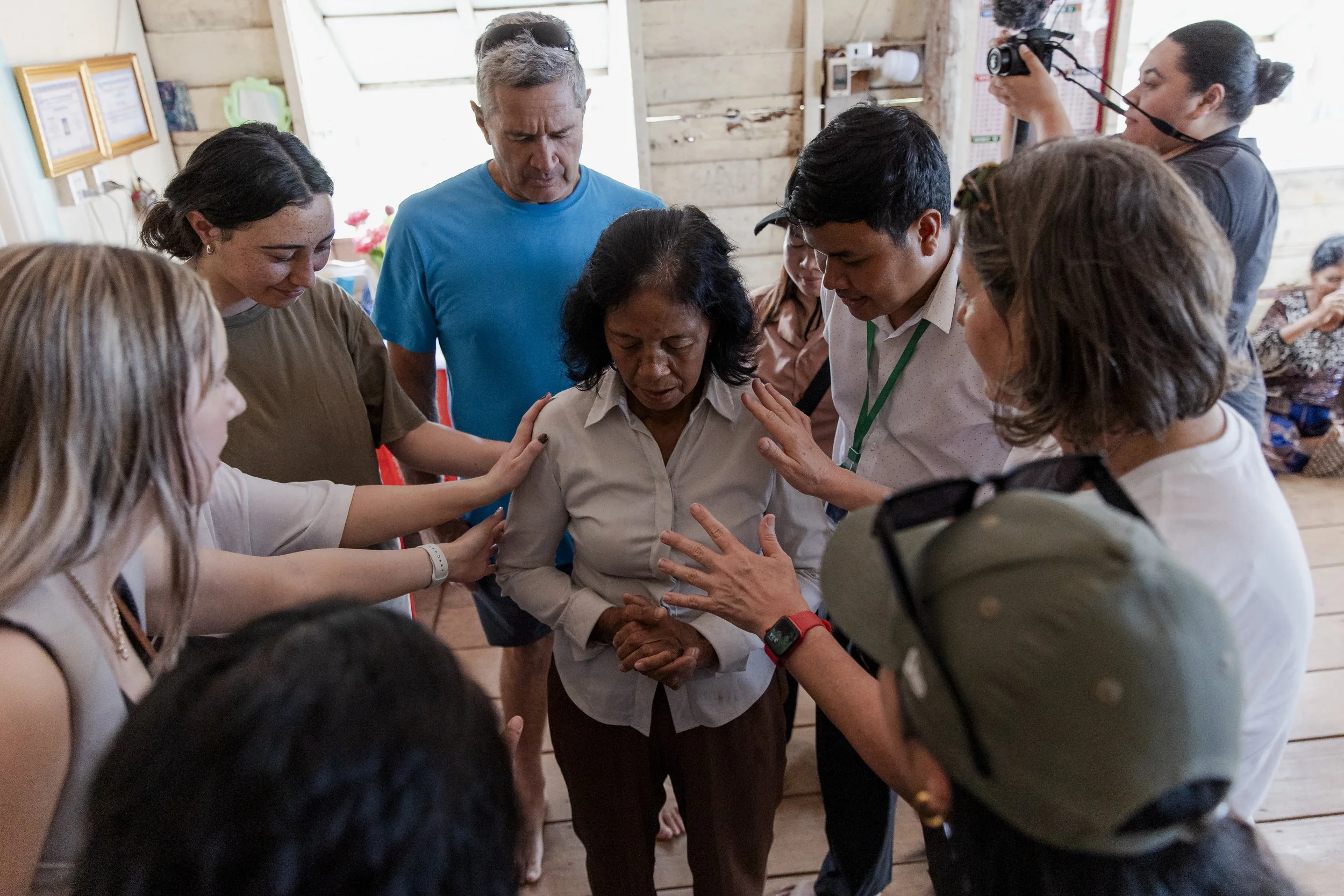 Group of people praying together inside a rustic wooden room.