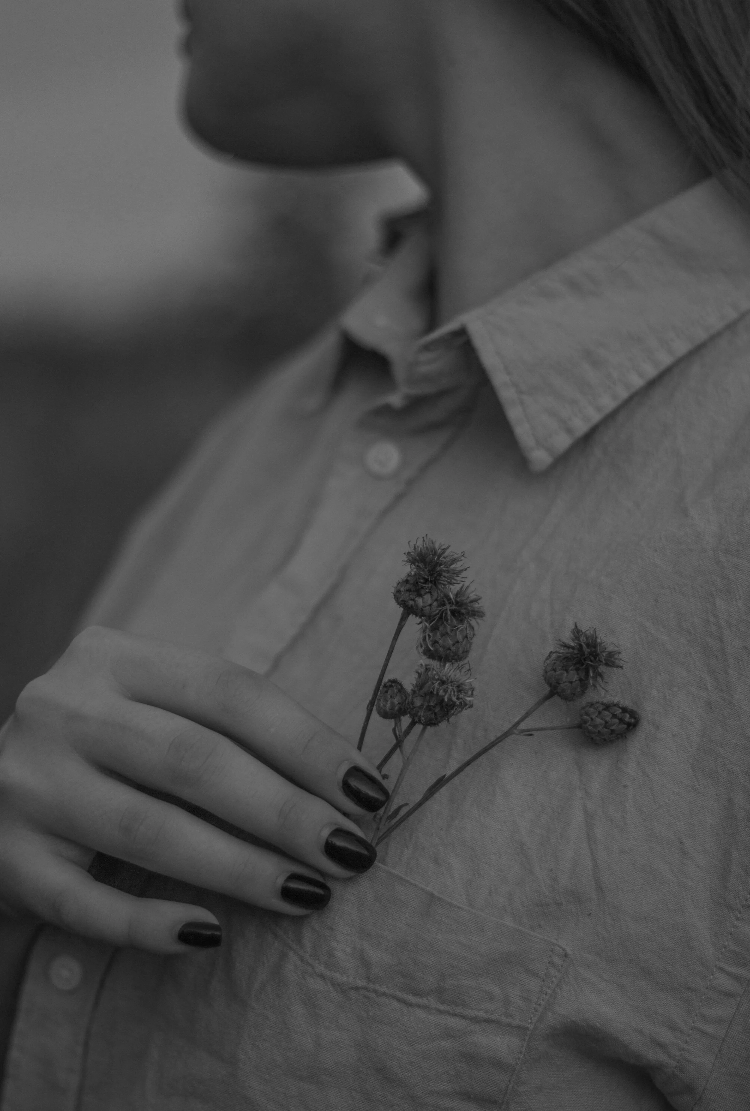 Close-up of a person holding a small bouquet of wildflowers and berries on their chest, wearing a light-colored button-up shirt.