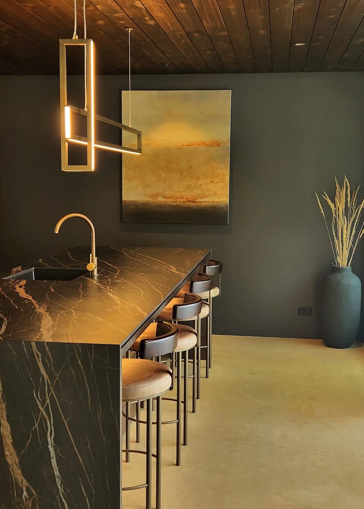 A designer kitchen island with dark marble, pendant light and artwork on the wall.