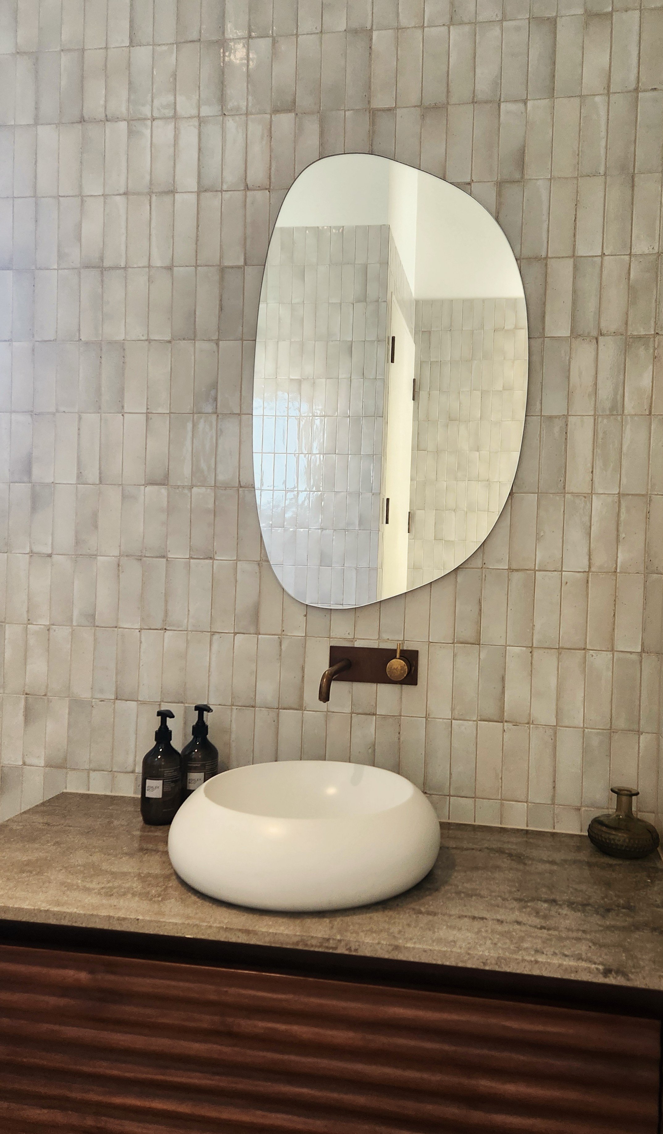 A tiled bathroom wall with bowl basin and designer mirror.