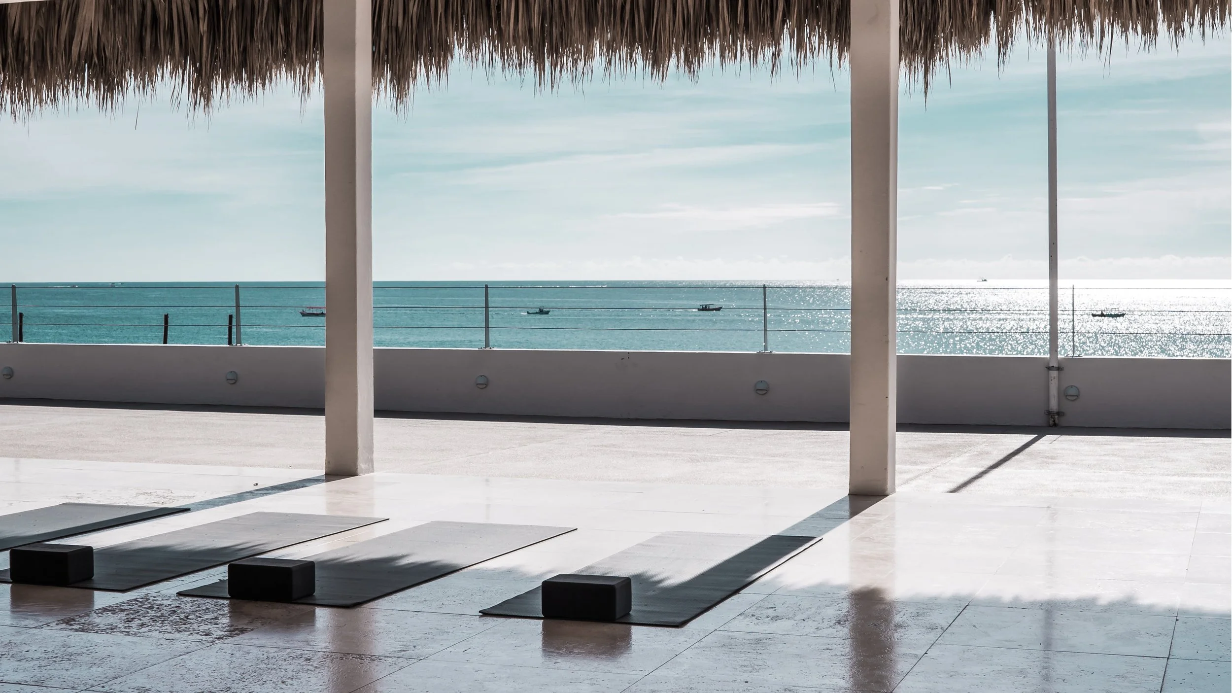 Yoga mats and blocks on a patio with ocean view and sailboats in the distance
