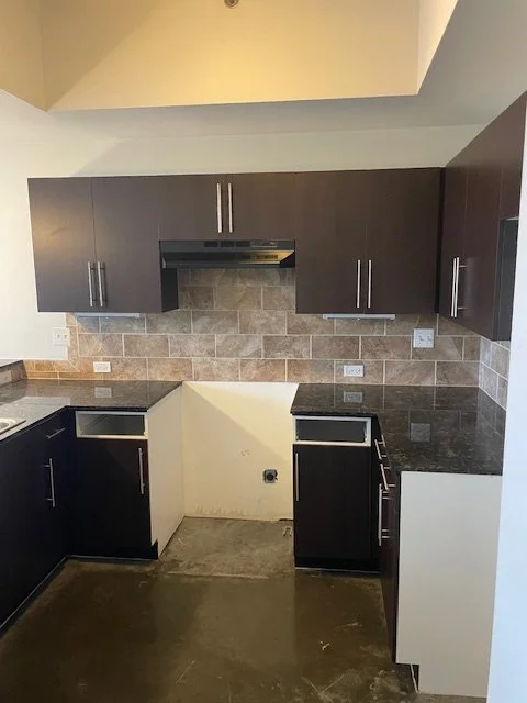 Empty kitchen with dark cabinets, granite countertops, tiled backsplash, and no appliances installed.