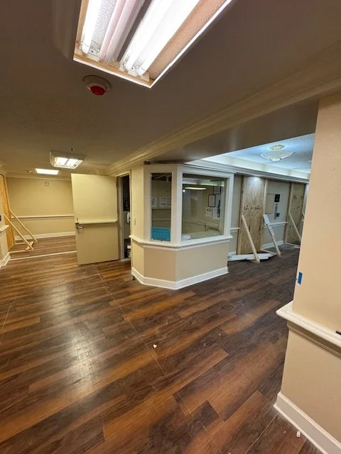 Interior of a building with hardwood floors, a skylight, and a glass-enclosed room or booth under construction.