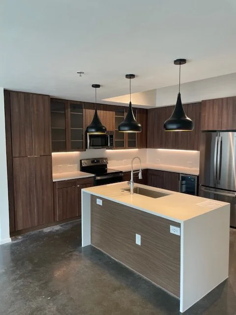 Modern kitchen with dark wood cabinets, stainless steel appliances, and a white island with a built-in sink and black pendant lights hanging above