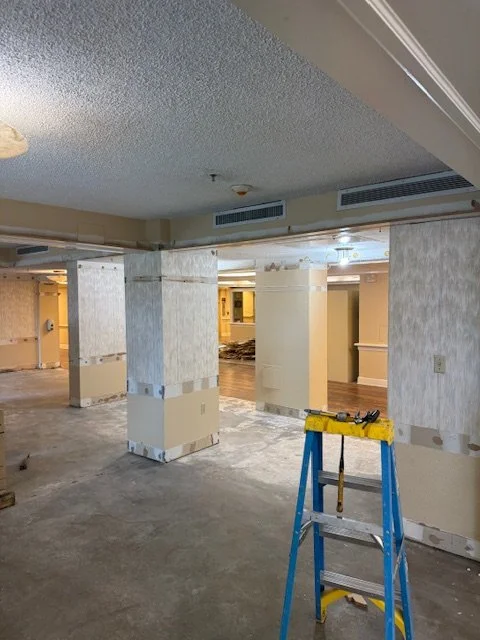 Interior space under renovation with partially finished walls, a blue stepladder, and construction tools.