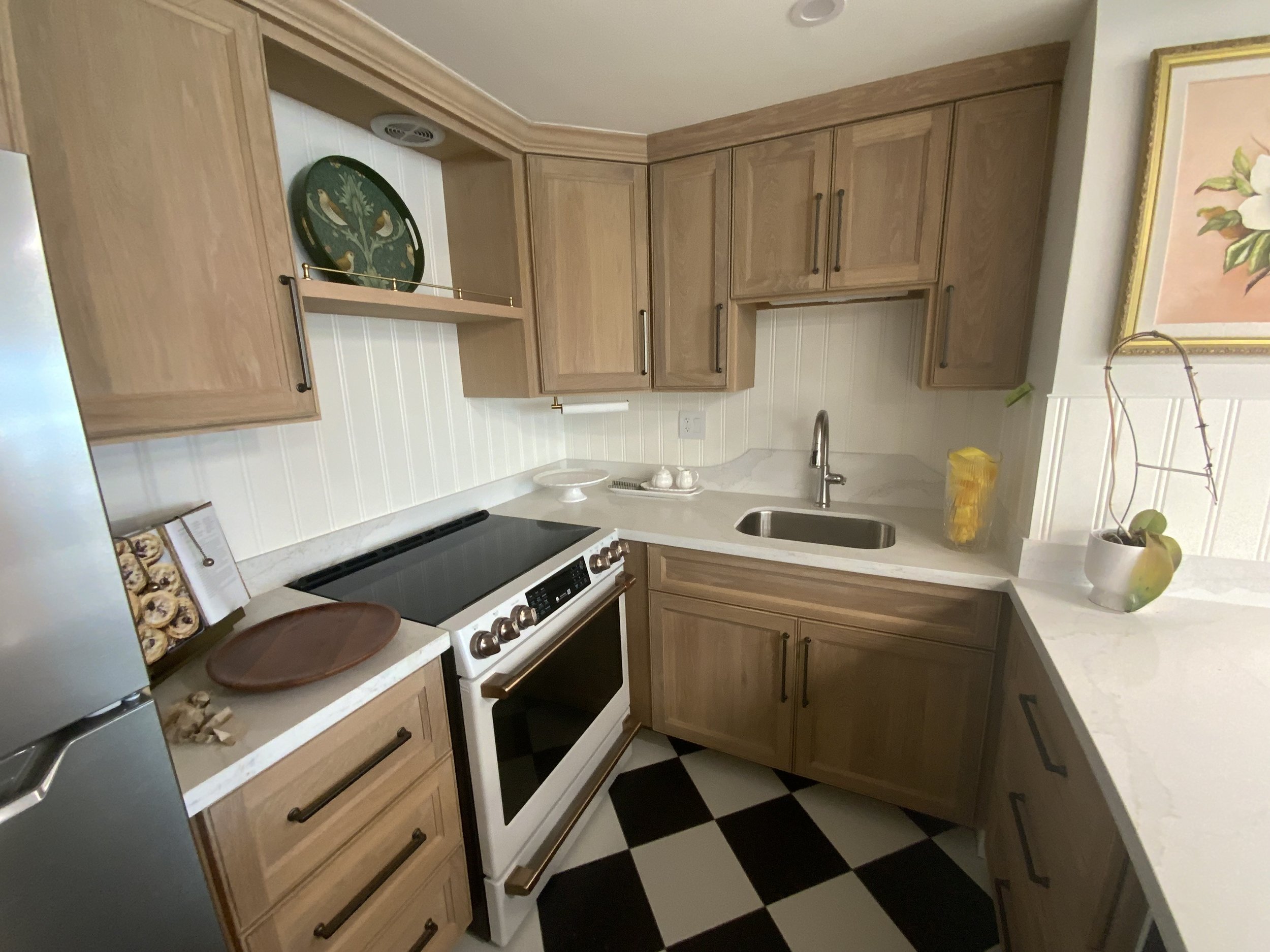A kitchen with wooden cabinets, a white stove, a black and white checkered floor, a laundry basket, a sink, and some decorative items.