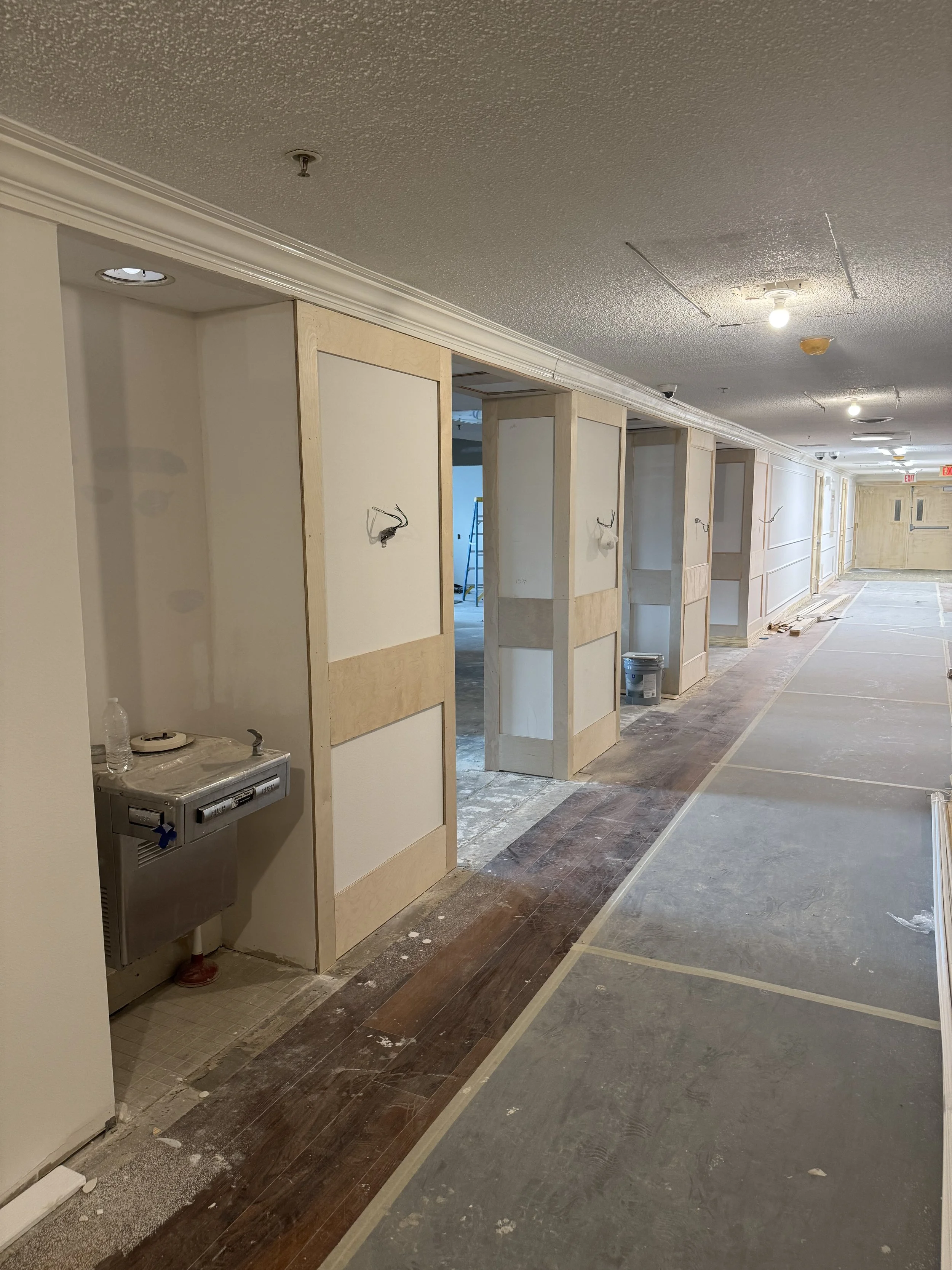 Hallway under construction with wood framing on walls, partially tiled floors, and visible electrical wiring.