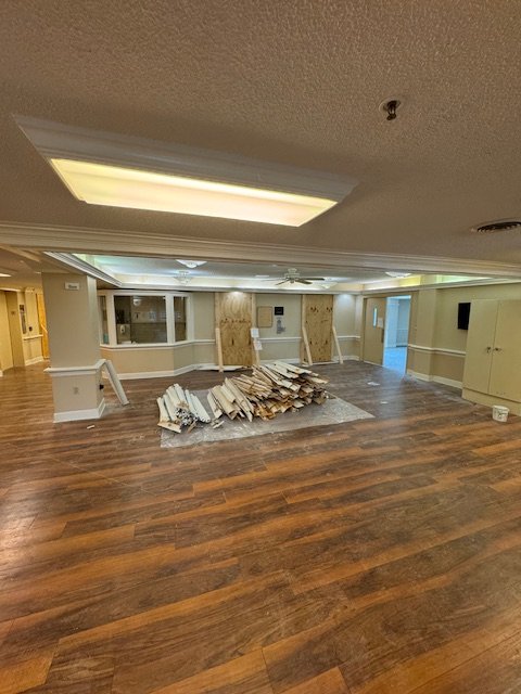 Empty room with stacked tiles or flooring materials on the floor, beige walls, ceiling with fluorescent lights, and a large window.