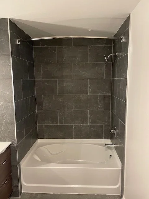 Bathroom with bathtub, dark gray tiled walls, and showerhead.