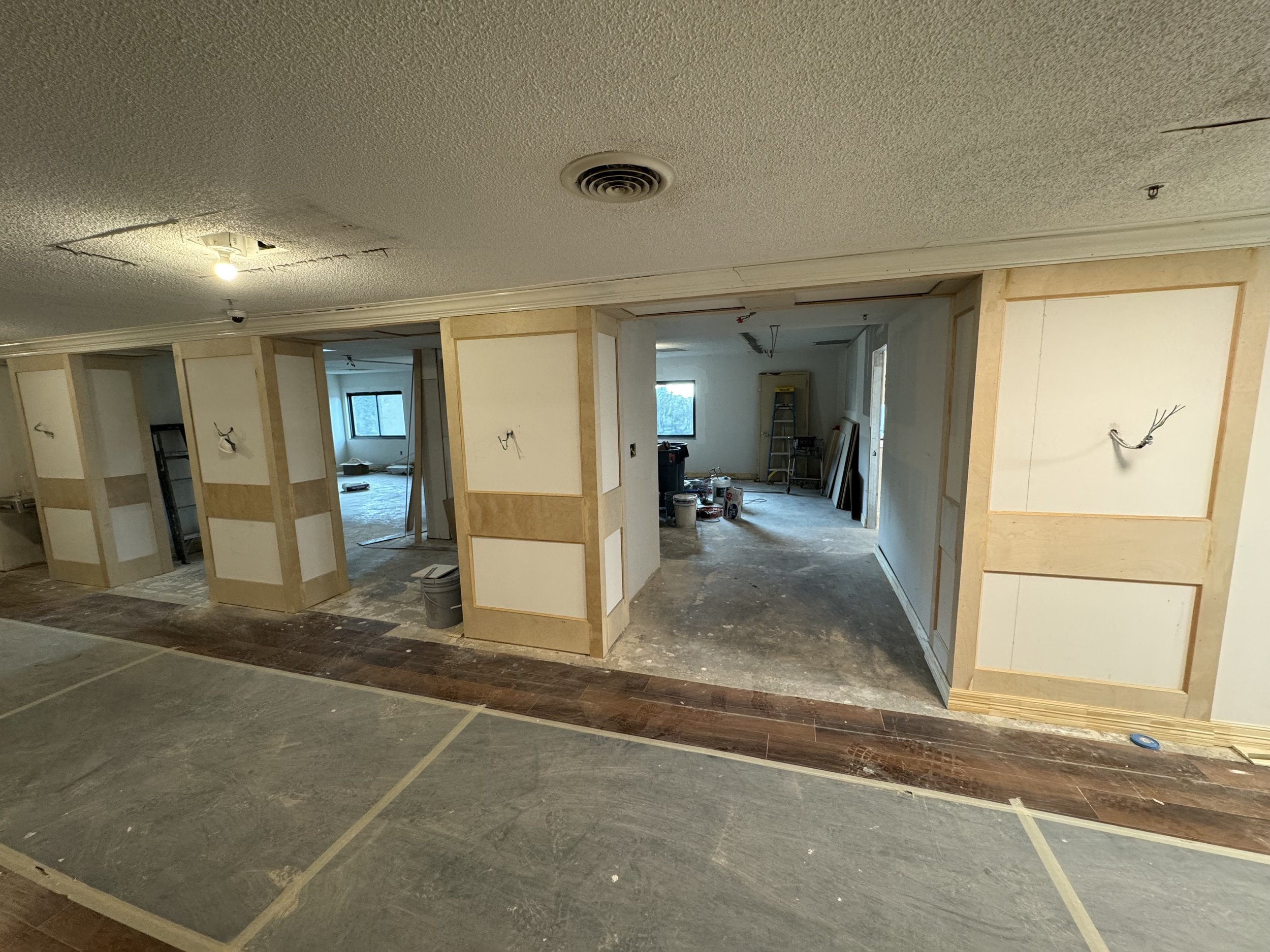 Interior of a building under construction with partially installed walls and exposed wiring, construction tools and ladders visible.