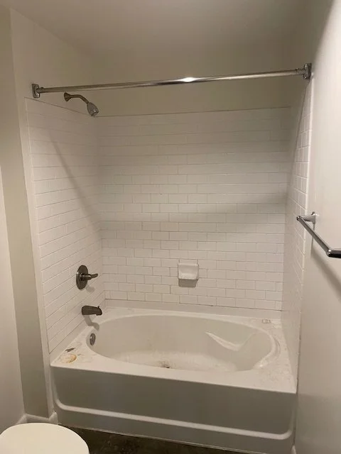 Empty bathtub in a bathroom with white tiled walls, a showerhead, a soap dish, a towel bar, and a shower curtain rod.