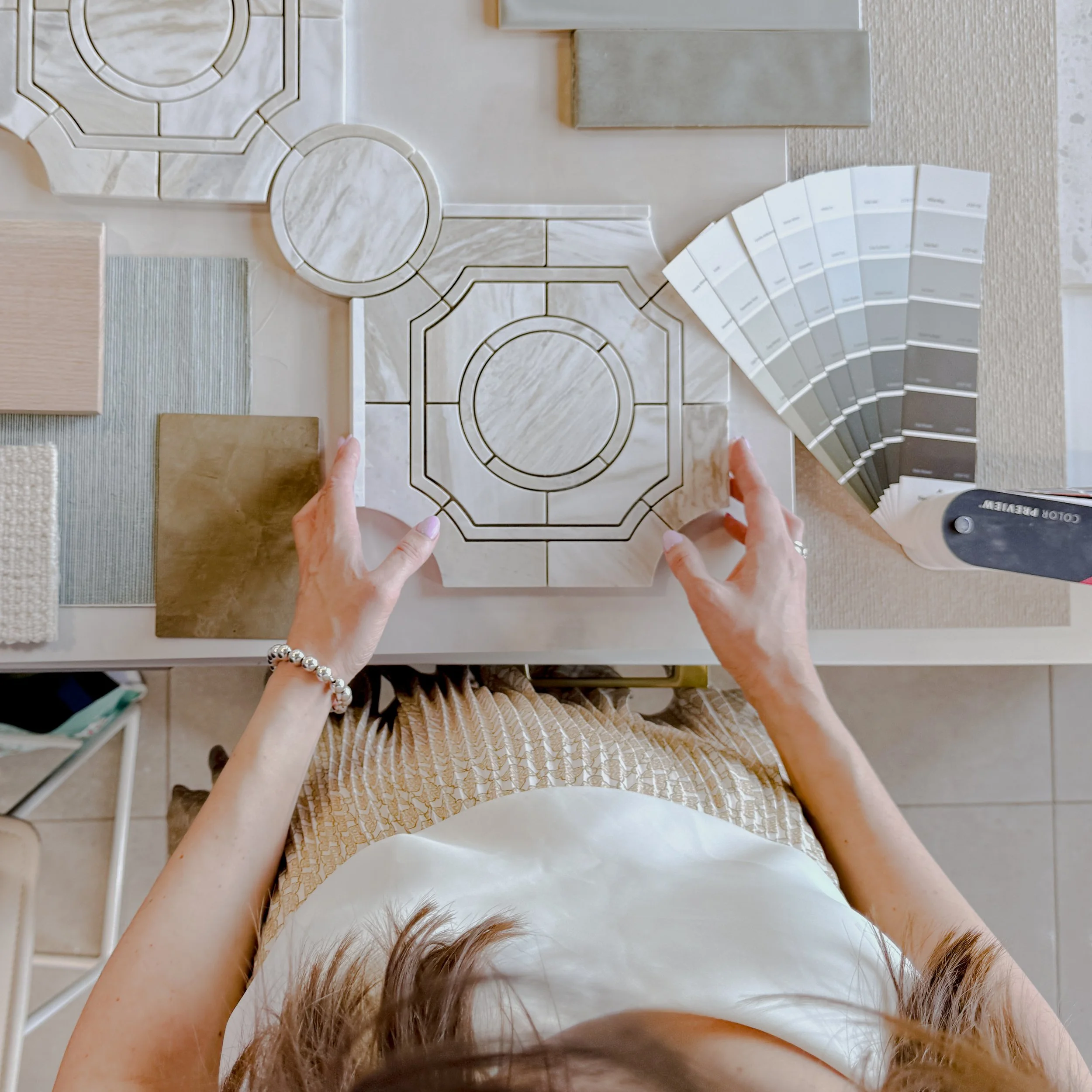 Top-down view of a person working on a tile design, with various color swatches and sample tiles on a table.