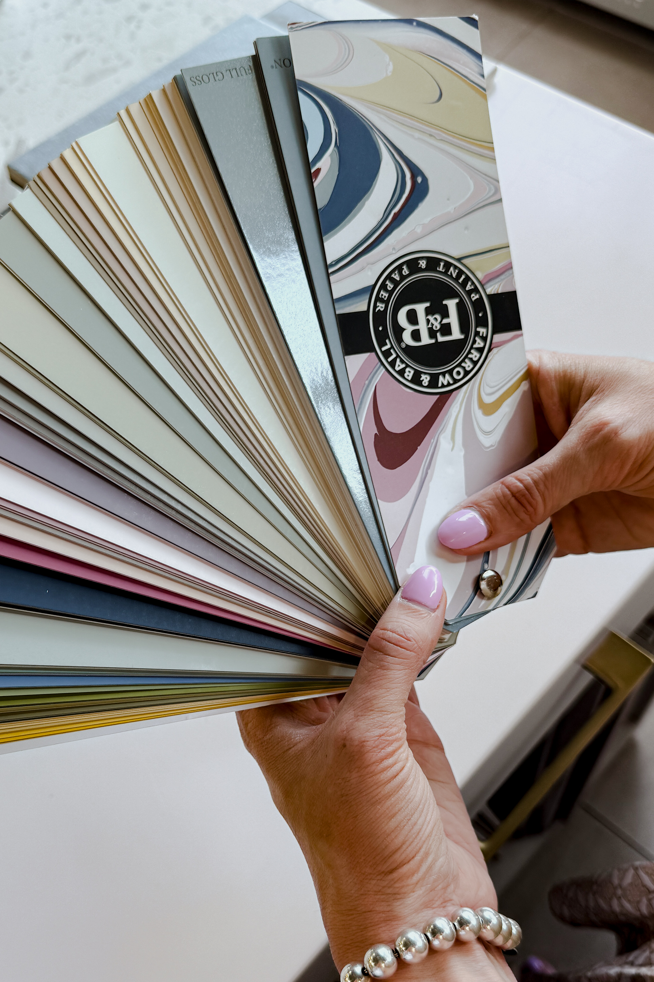 A person holding a fan deck of paint color swatches with various shades and finishes.